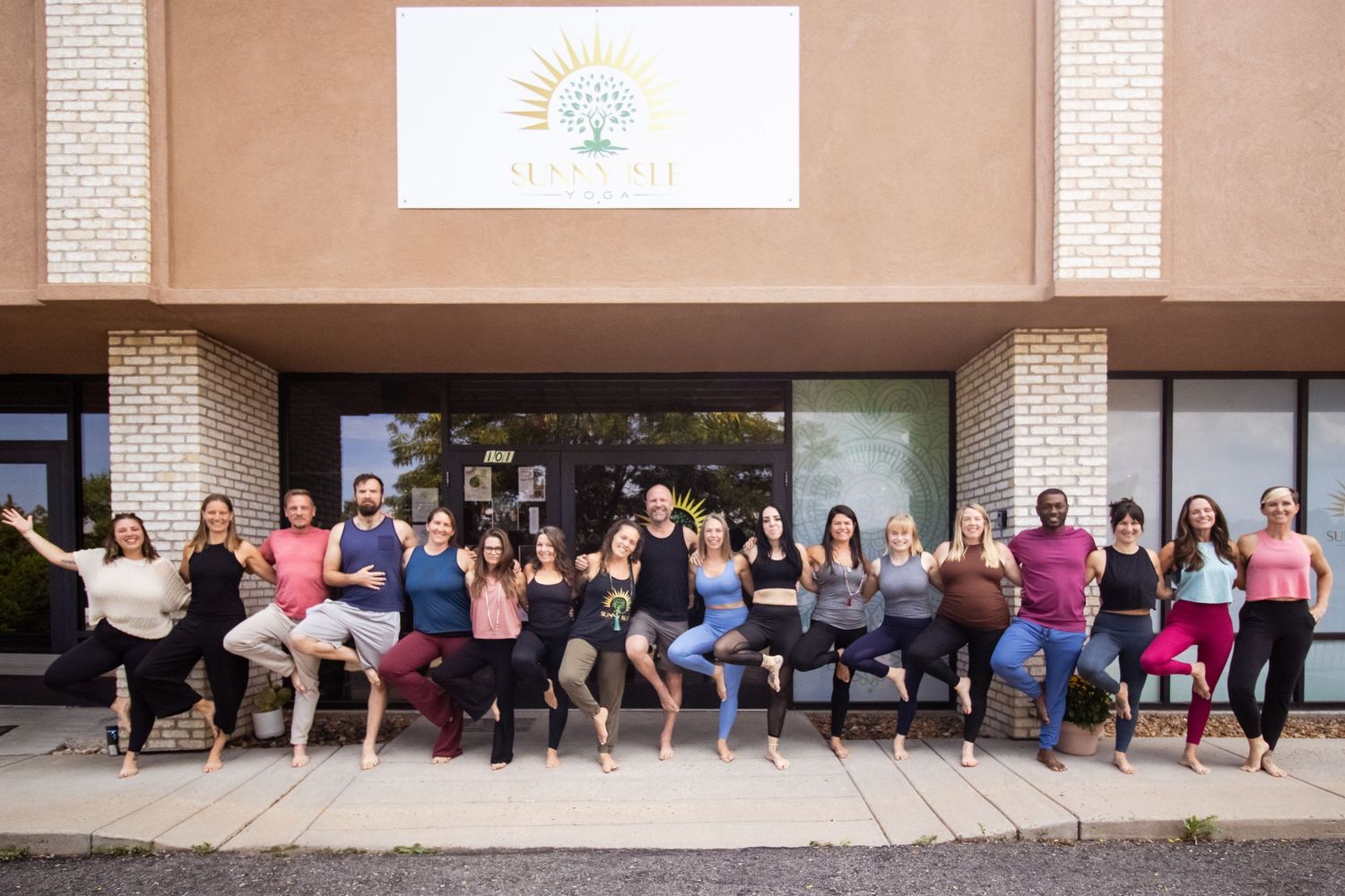 Large group of people in workout attire lined up against a brick wall outside a fitness studio.