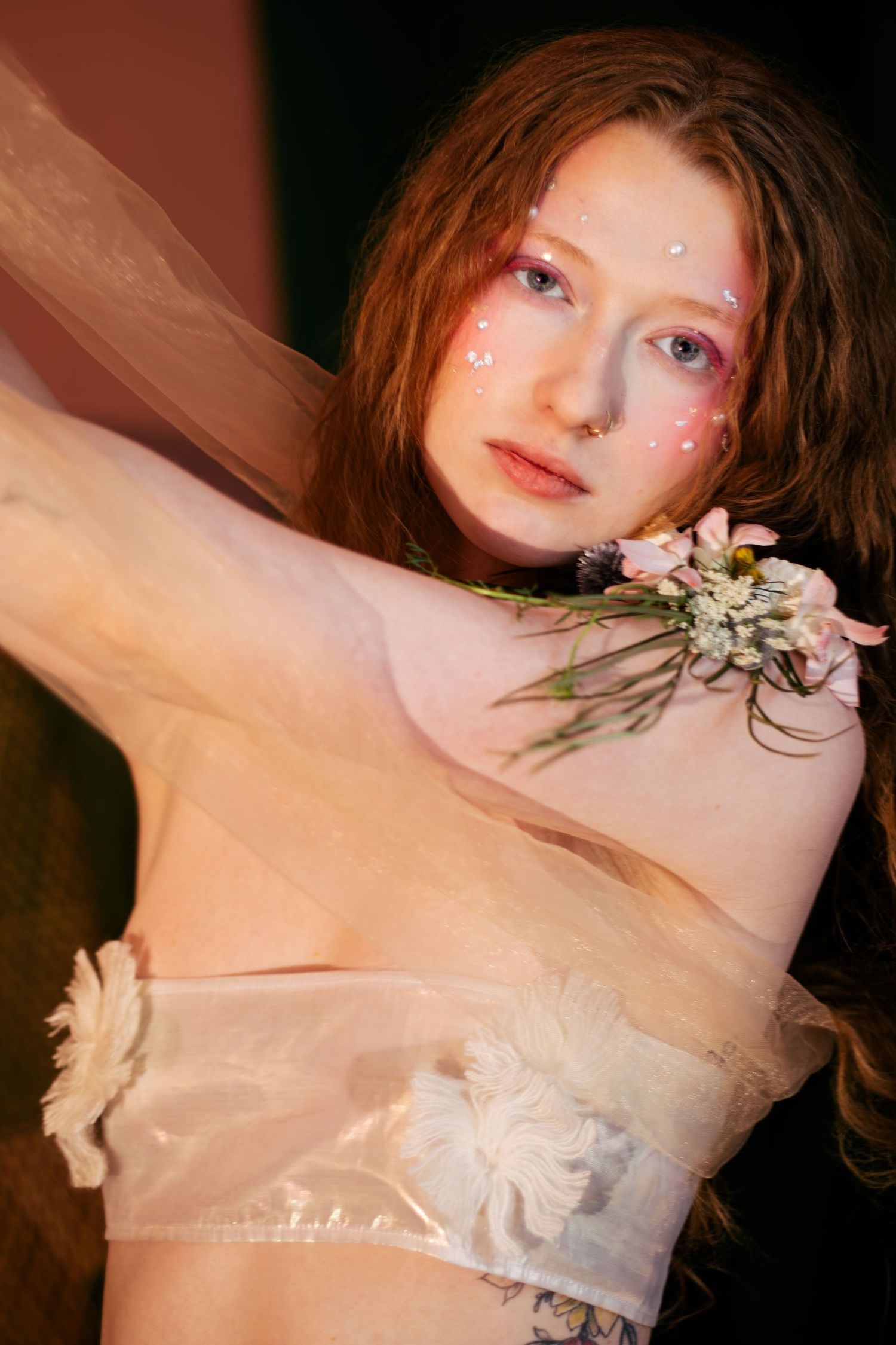 Dreamy portrait with delicate flowers and sheer white fabric against dark background.