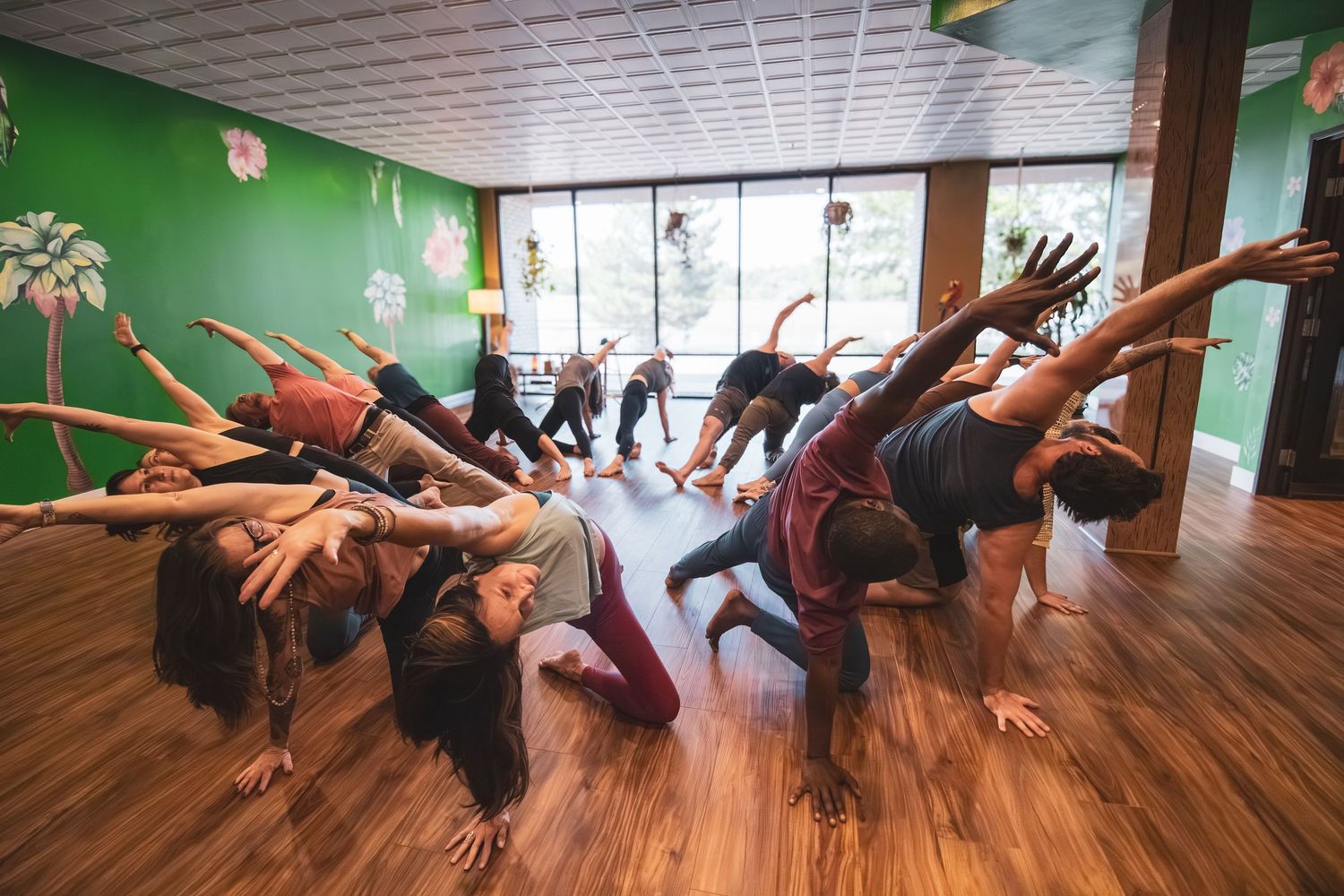 A group of dancers performing a synchronized movement in a bright dance studio with wooden floors.