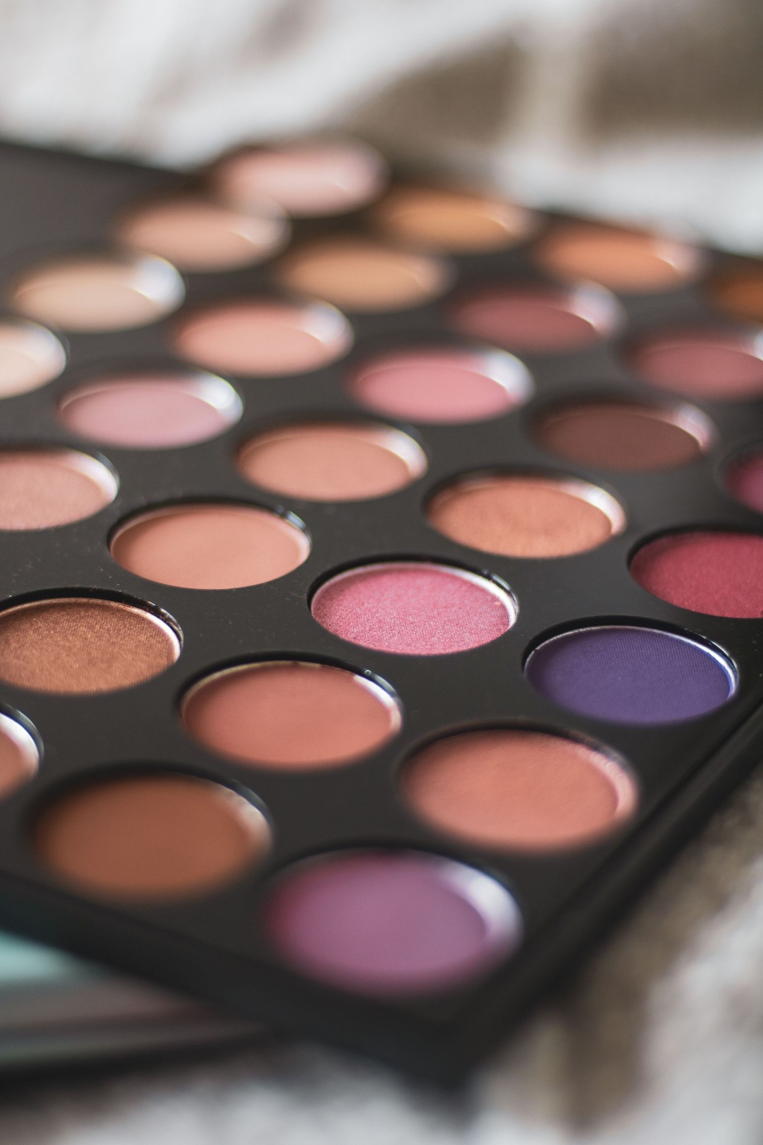 Close-up view of a professional makeup palette showing pink, purple, and neutral eyeshadow shades in circular pans.