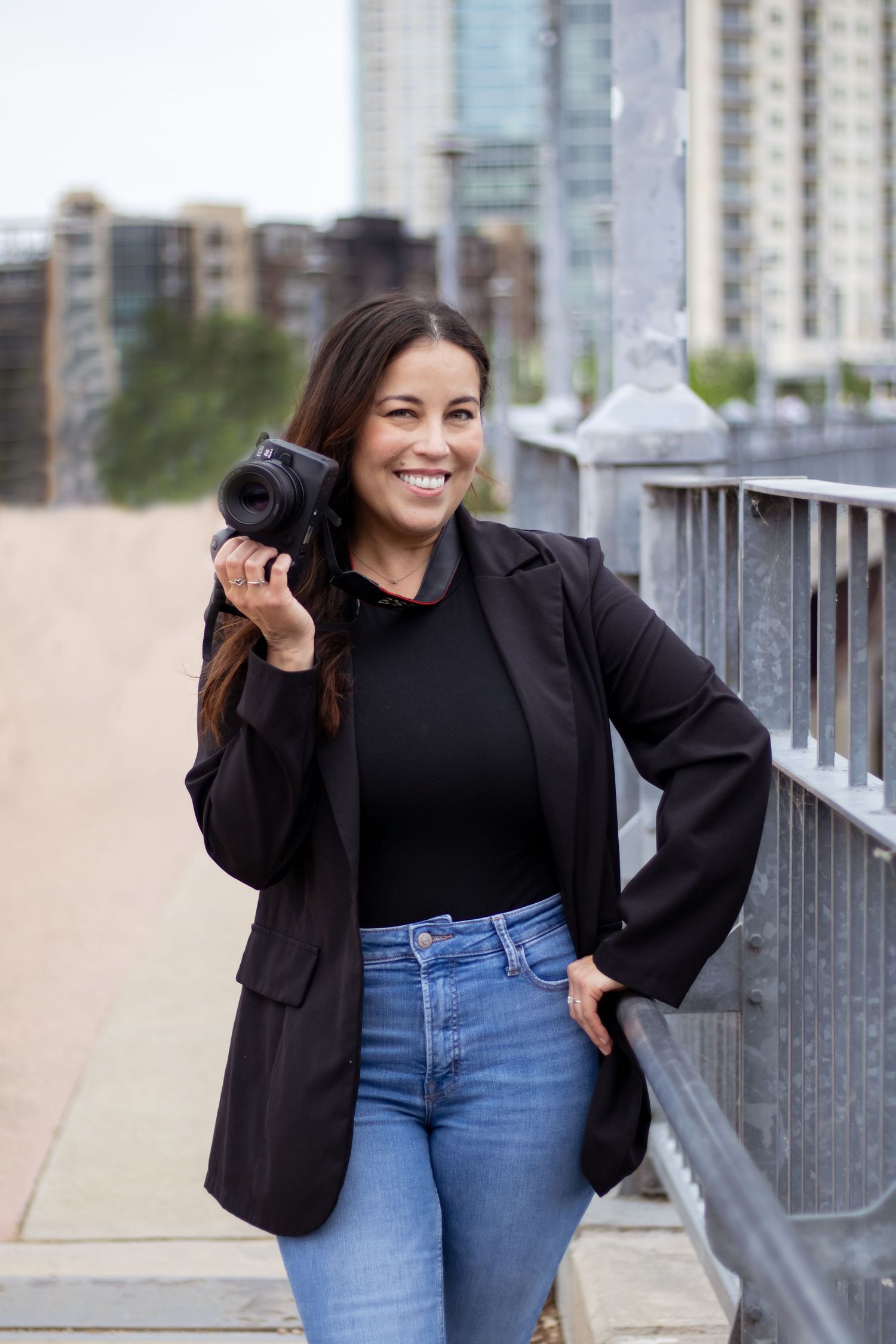 Person in black top and jeans posing confidently on urban rooftop or balcony.