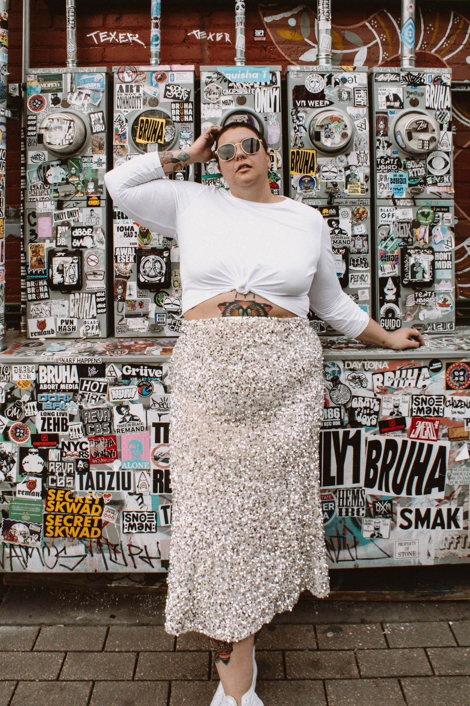 A sequence of four photos showing a person in a white top and patterned skirt posing against a wall covered in stickers.