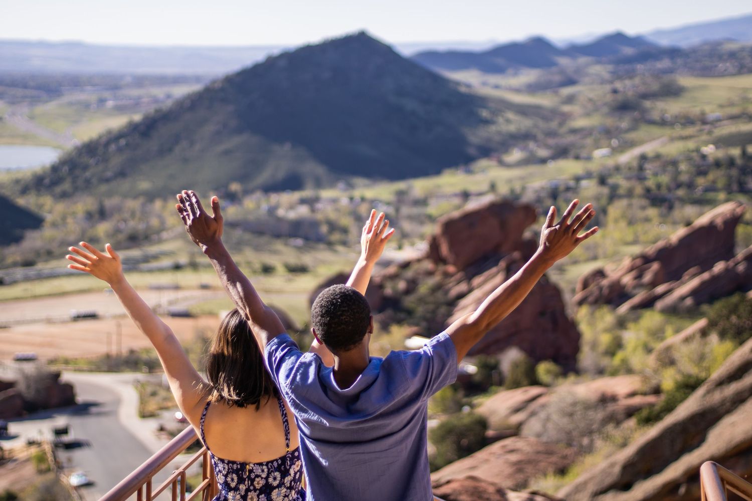 People with raised arms celebrating at Red Rocks Amphitheatre in Colorado against a backdrop of scenic mountains.