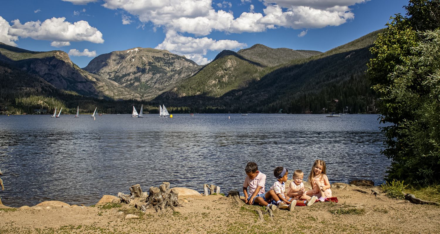 Panoramic view of a mountain lake surrounded by peaks and green forests under a blue sky with white clouds.