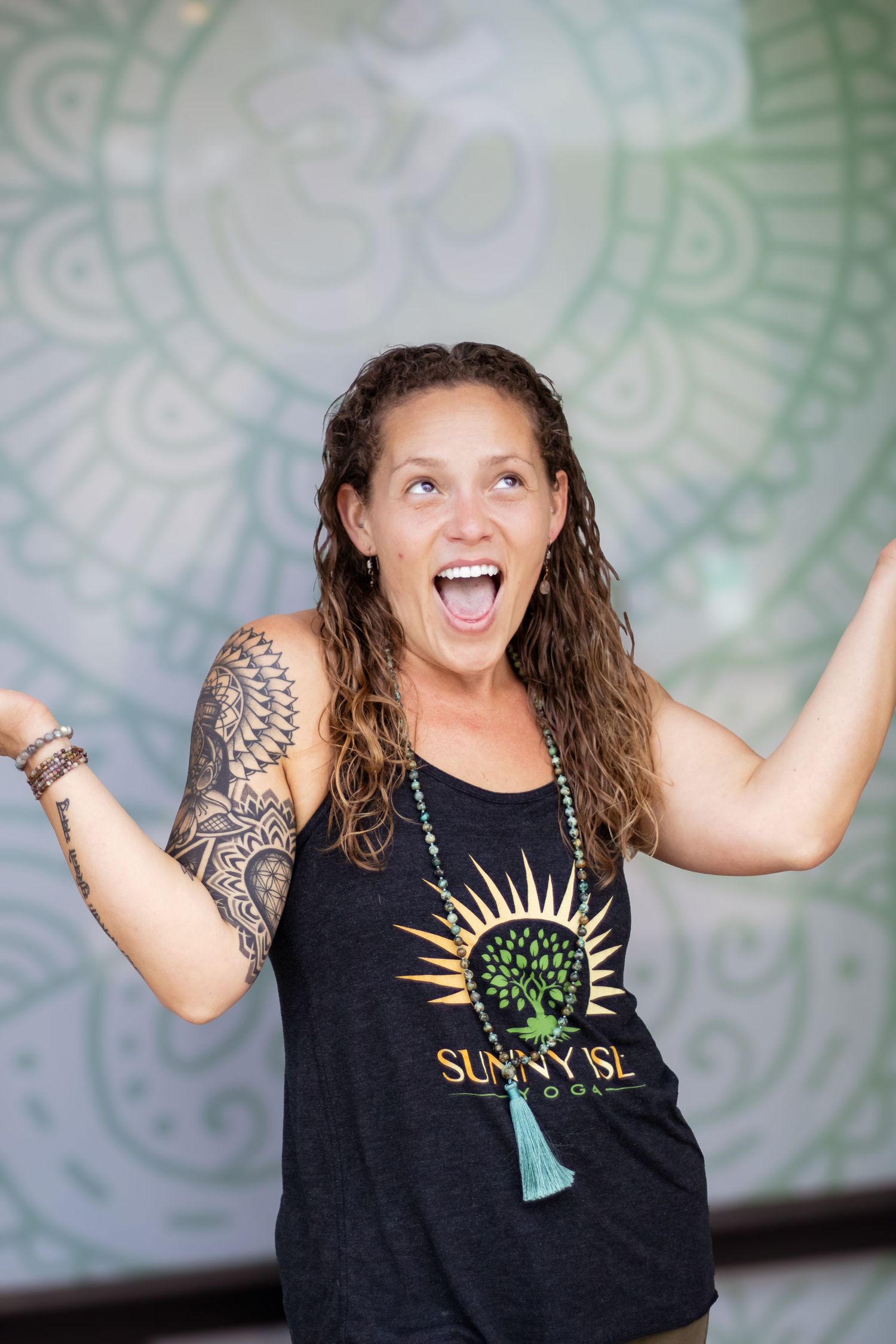 Excited person with wet hair and tattoos wearing a Sunny Side tank top poses energetically against a patterned wall.