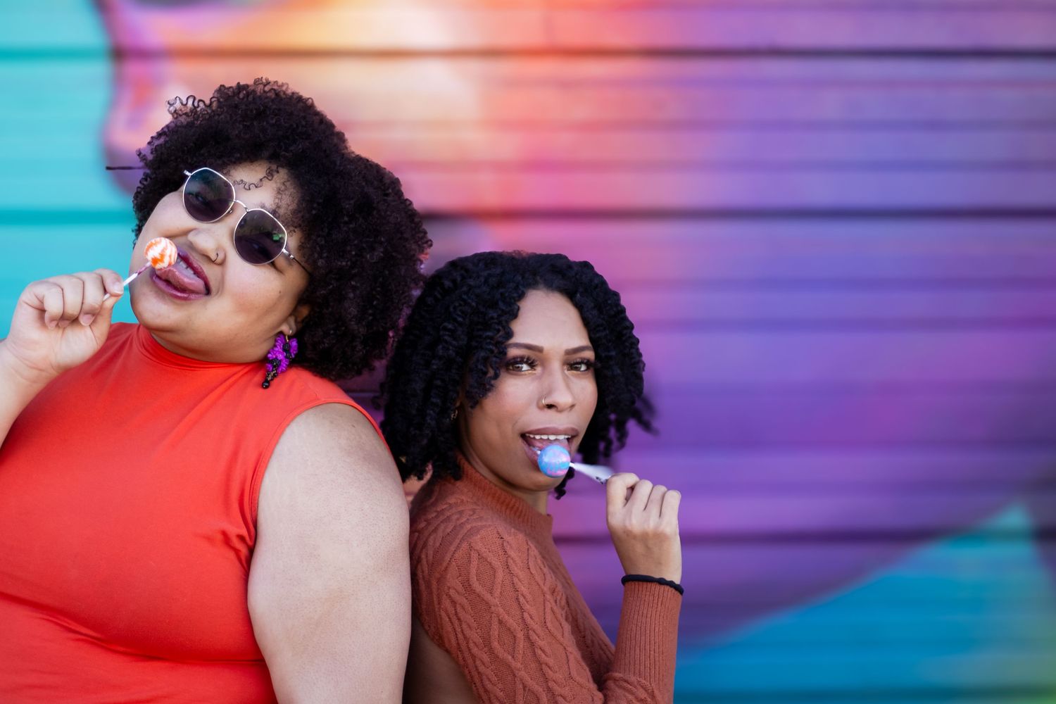 Two friends laughing and having fun against a colorful gradient background with vibrant pink and blue lighting.