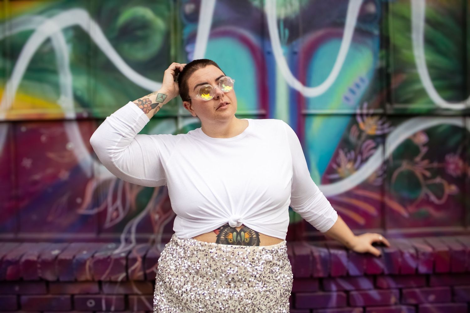 A person in a white shirt poses in front of a colorful graffiti wall with dynamic movement and style.