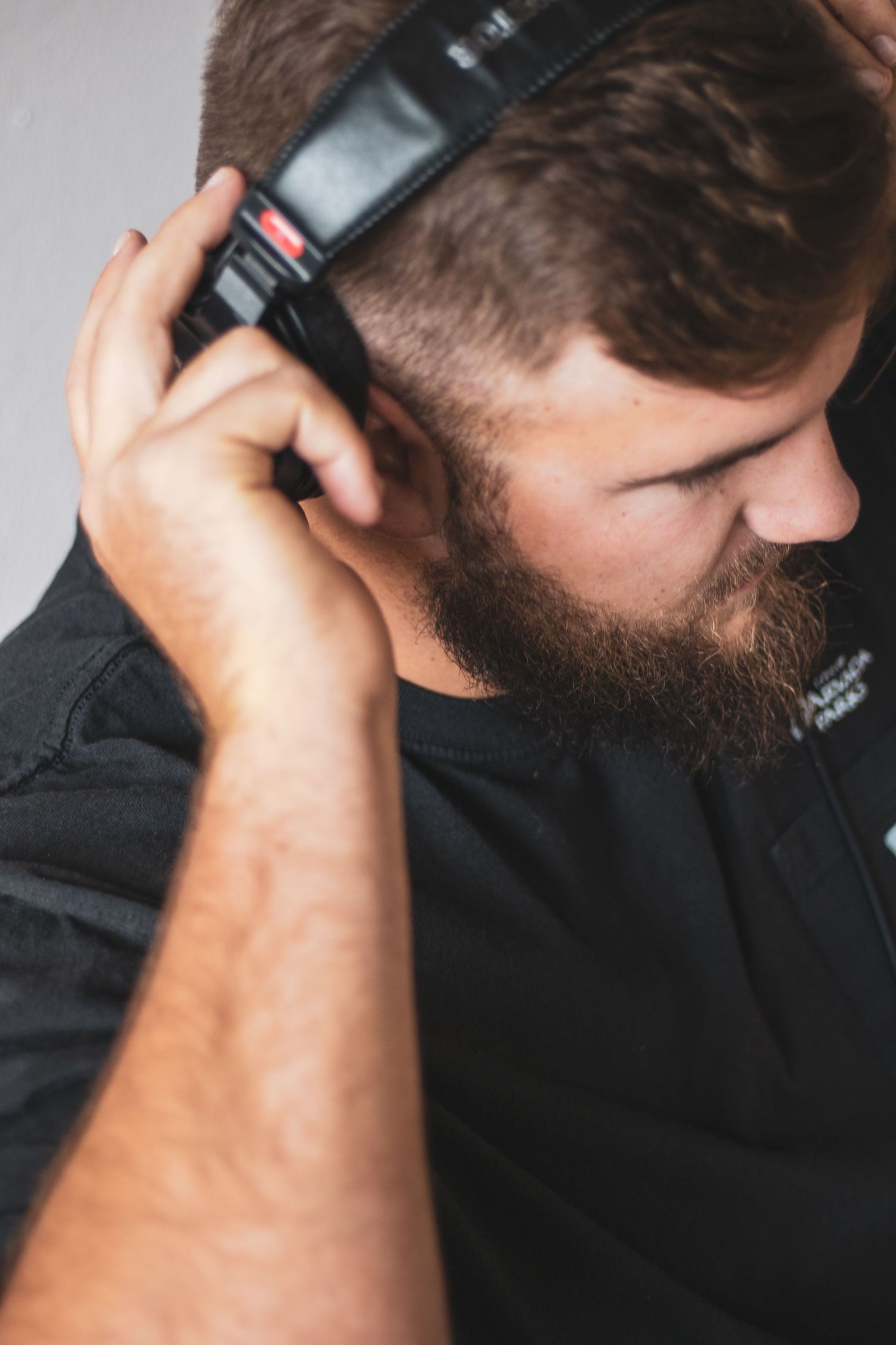 A person wearing black headphones with a full beard listens intently while wearing a dark t-shirt.