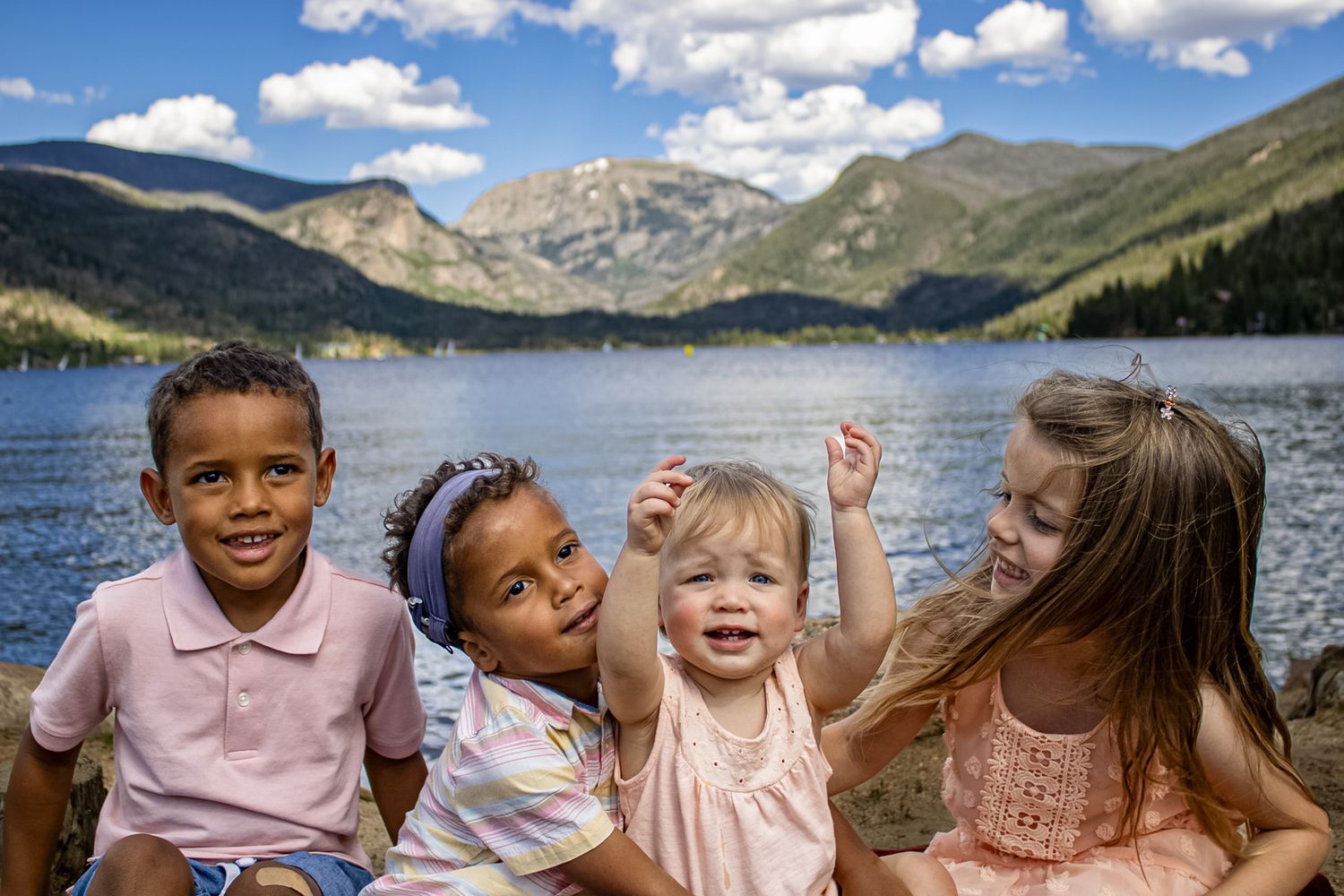 Happy group portrait of family members by a mountain lake on a bright summer day.
