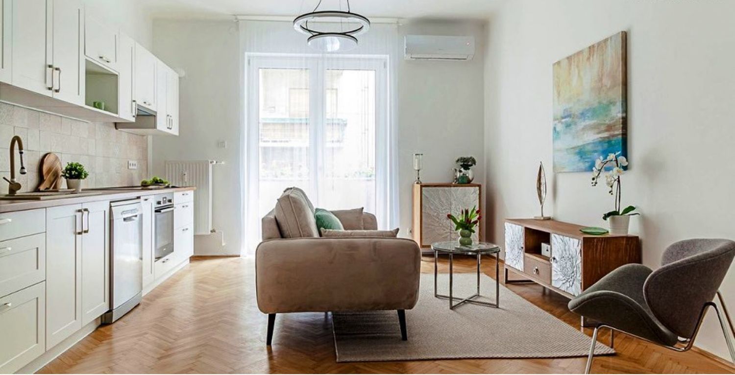 Modern open-plan studio apartment with white kitchen, herringbone parquet floor, and neutral Scandinavian decor.
