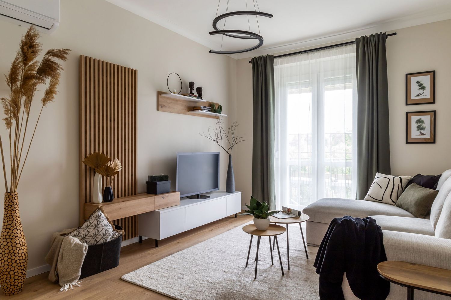 Modern living room with wooden TV unit, gray sofa, round coffee tables, and large balcony windows.