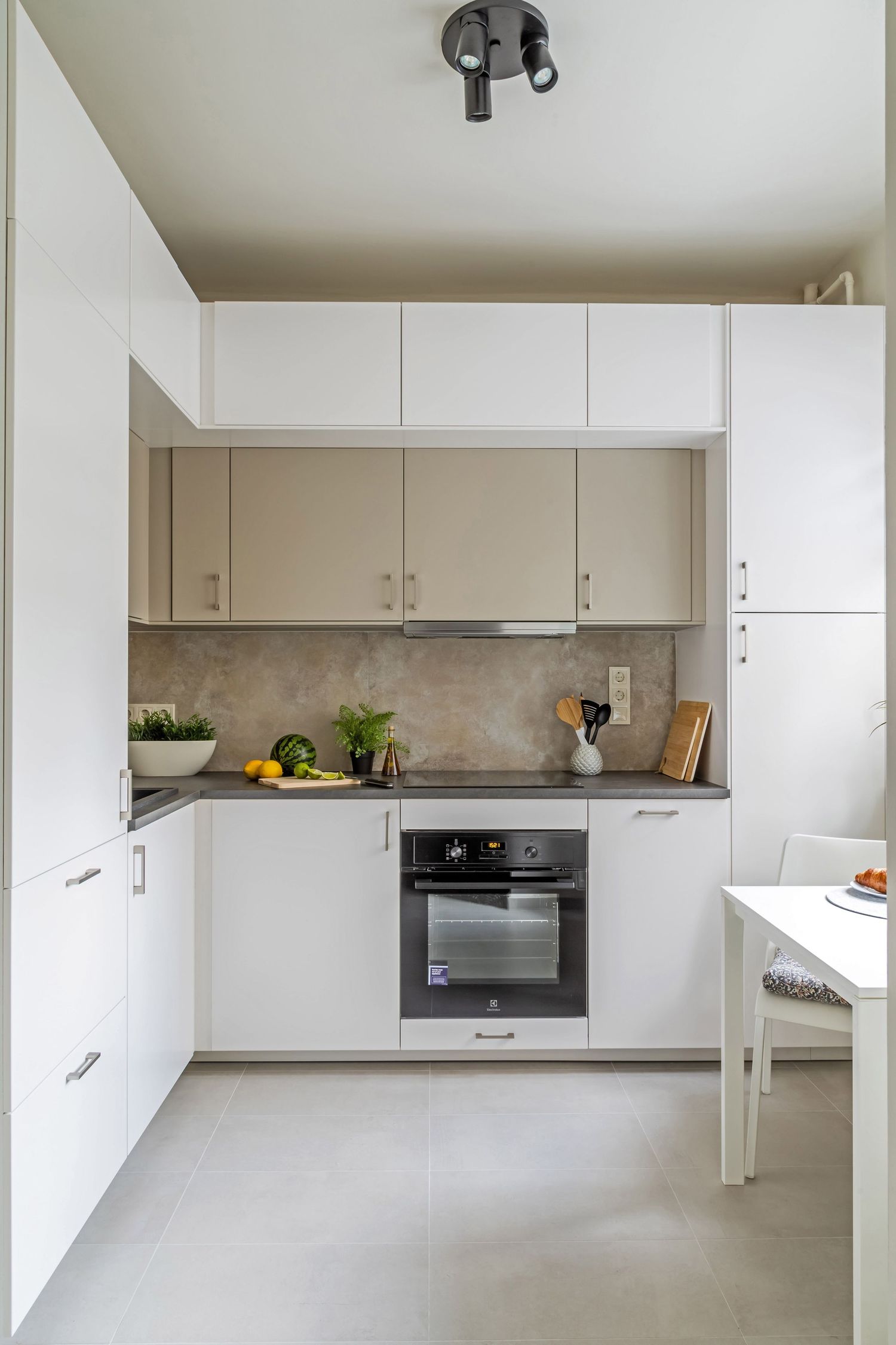 Compact modern kitchen with white cabinetry, beige upper cabinets, stone backsplash, and built-in oven.
