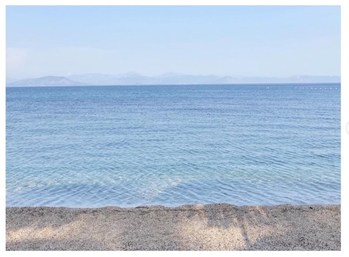 Crystal clear turquoise Mediterranean sea viewed from a stone waterfront promenade with distant mountains.
