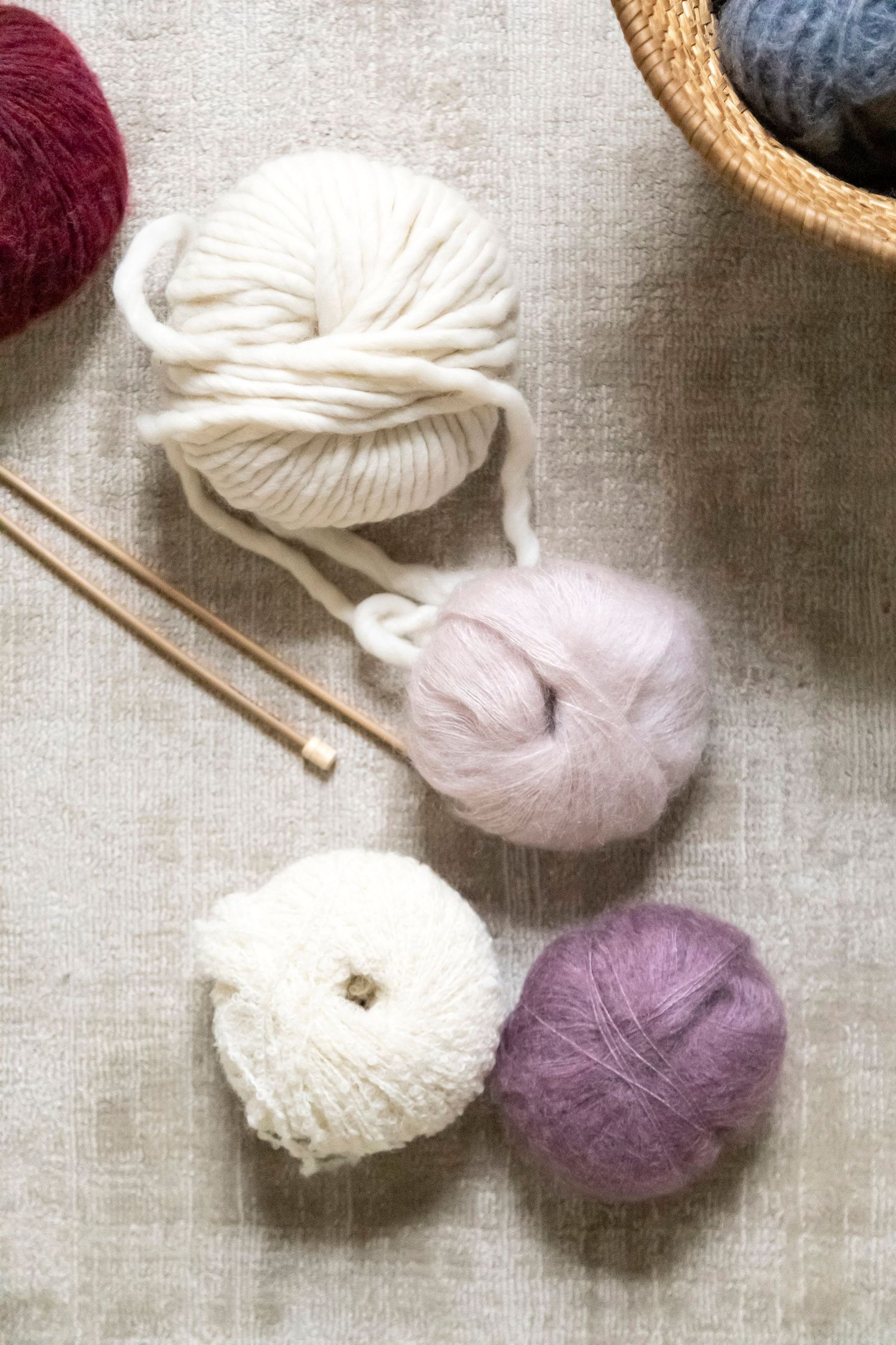 Assorted balls of yarn in white, pink, and purple with wooden knitting needles on linen.