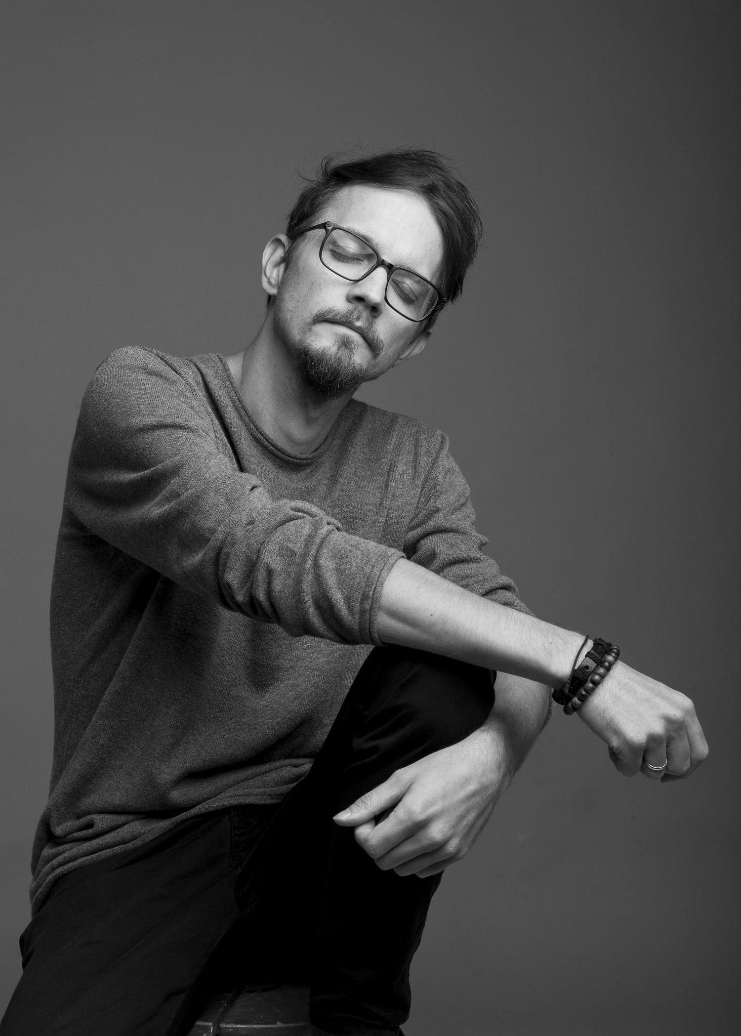 Black and white photo of man in gray sweater and glasses posing dynamically while seated.