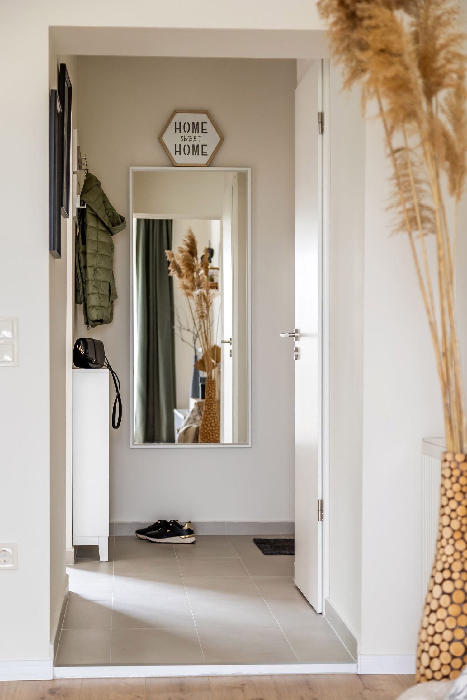Bright apartment entryway with full-length mirror, coat hooks, white shoe cabinet, and a Home Sweet Home sign.