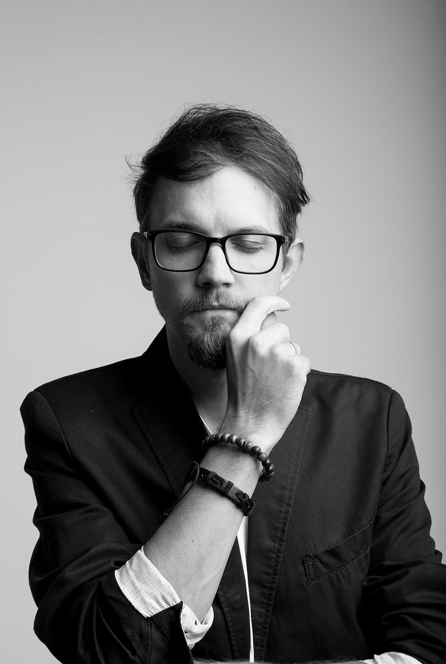 Black and white portrait of a thoughtful man with glasses and beard, hand on chin in contemplative pose.