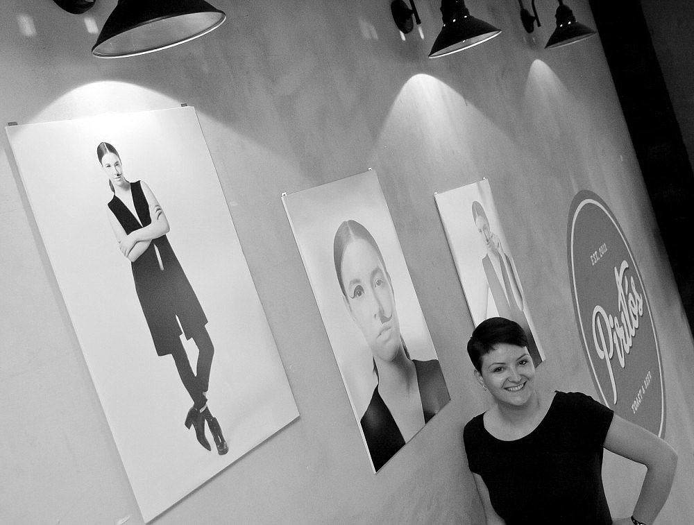 Woman smiling beside large black and white portrait photographs displayed on a wall in a gallery.