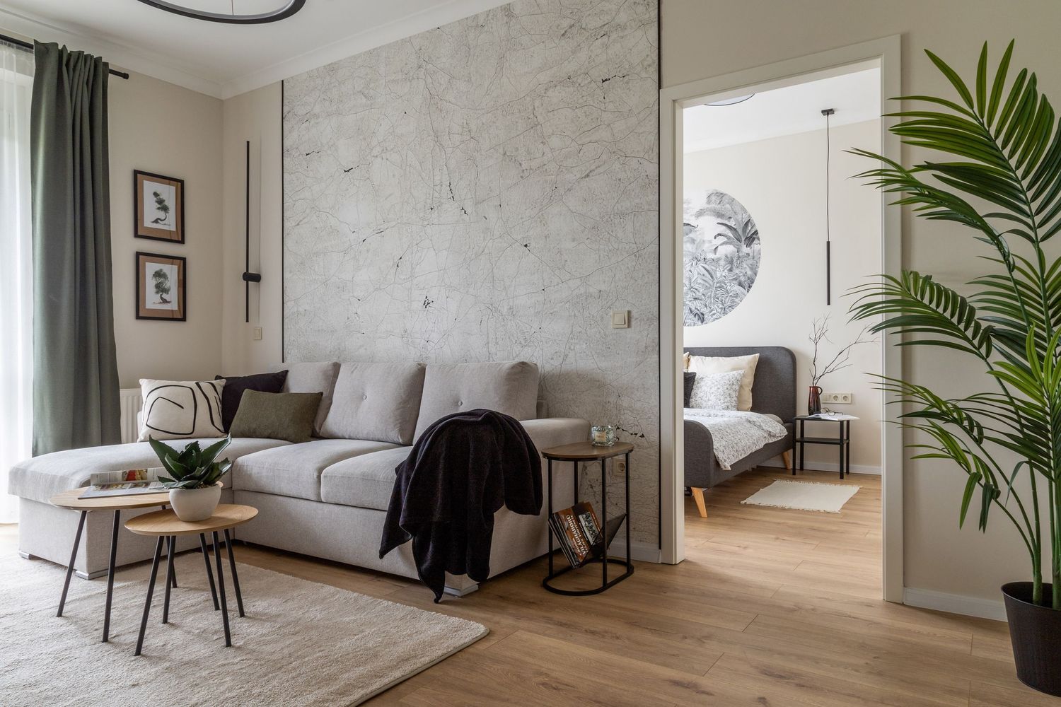 Modern living room with grey sofa, marble accent wall, and open doorway leading to a bright bedroom with wooden floors.