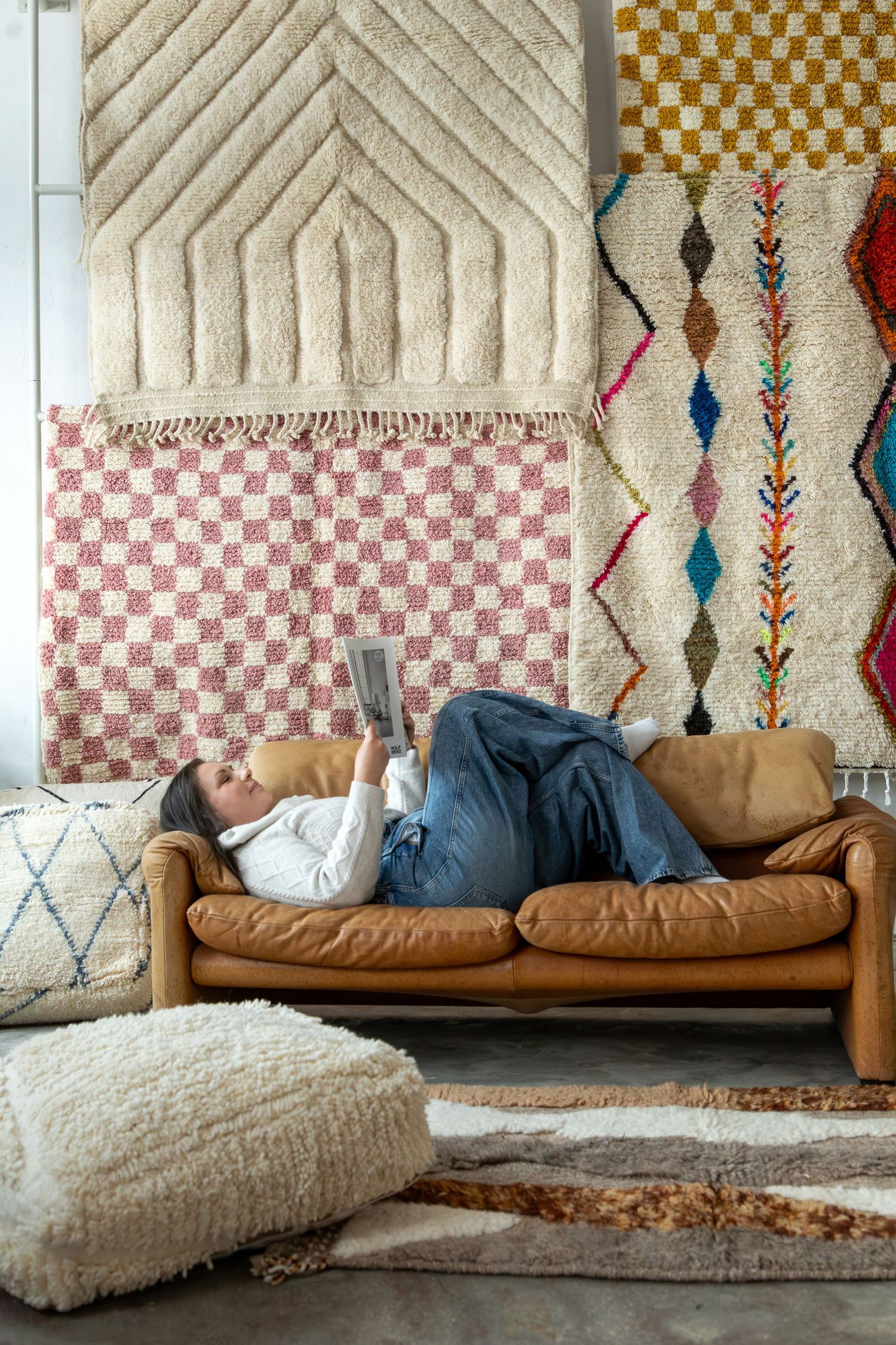 Woman lying on a tan leather sofa reading, surrounded by colorful Moroccan rugs on the wall and floor.