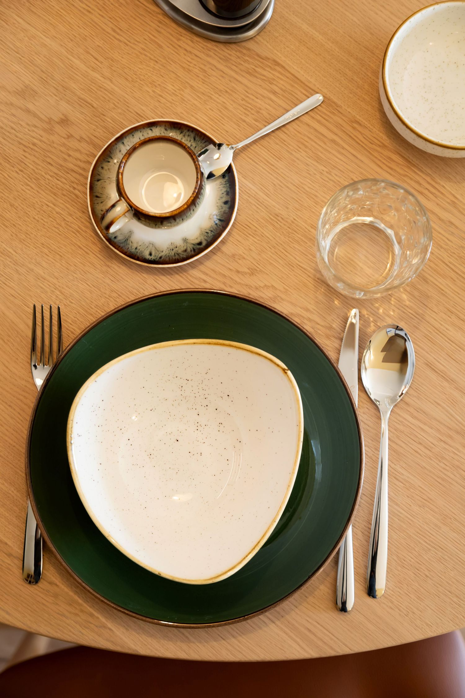 Elegant restaurant place setting with green and white plates, silver cutlery, and a coffee cup on a wooden table.