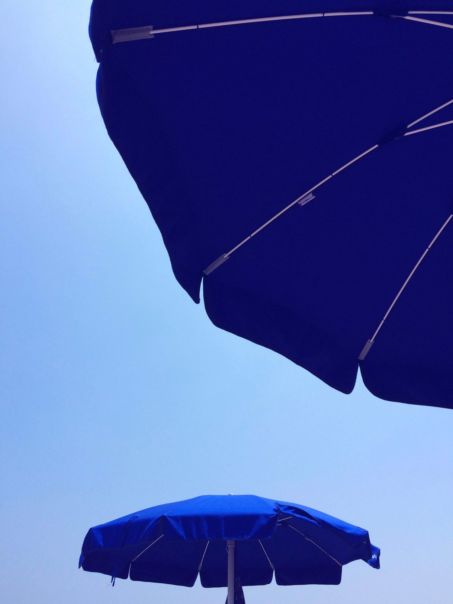 Two vibrant blue beach umbrellas against a clear blue sky, viewed from below on a sunny day.