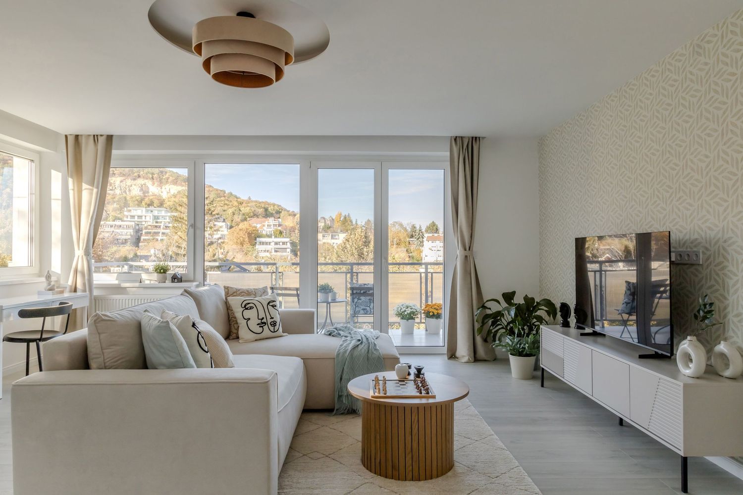 Modern bright living room with large windows overlooking a lake, featuring a neutral sofa and wood table.