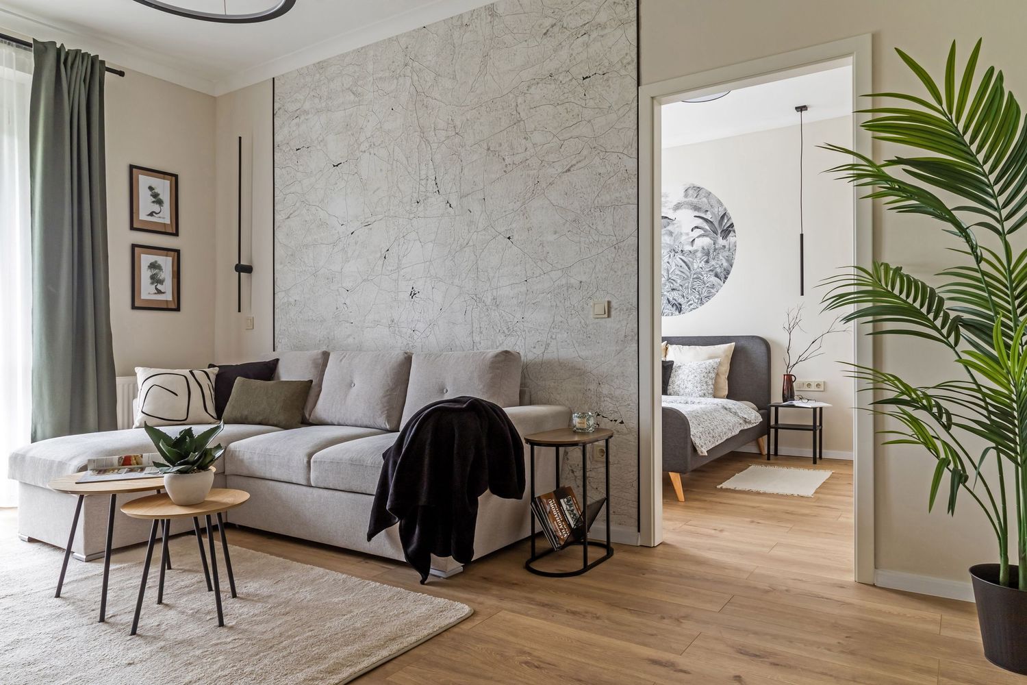 Scandinavian living room with gray sofa, marble accent wall, black side tables, and a view into the bedroom.