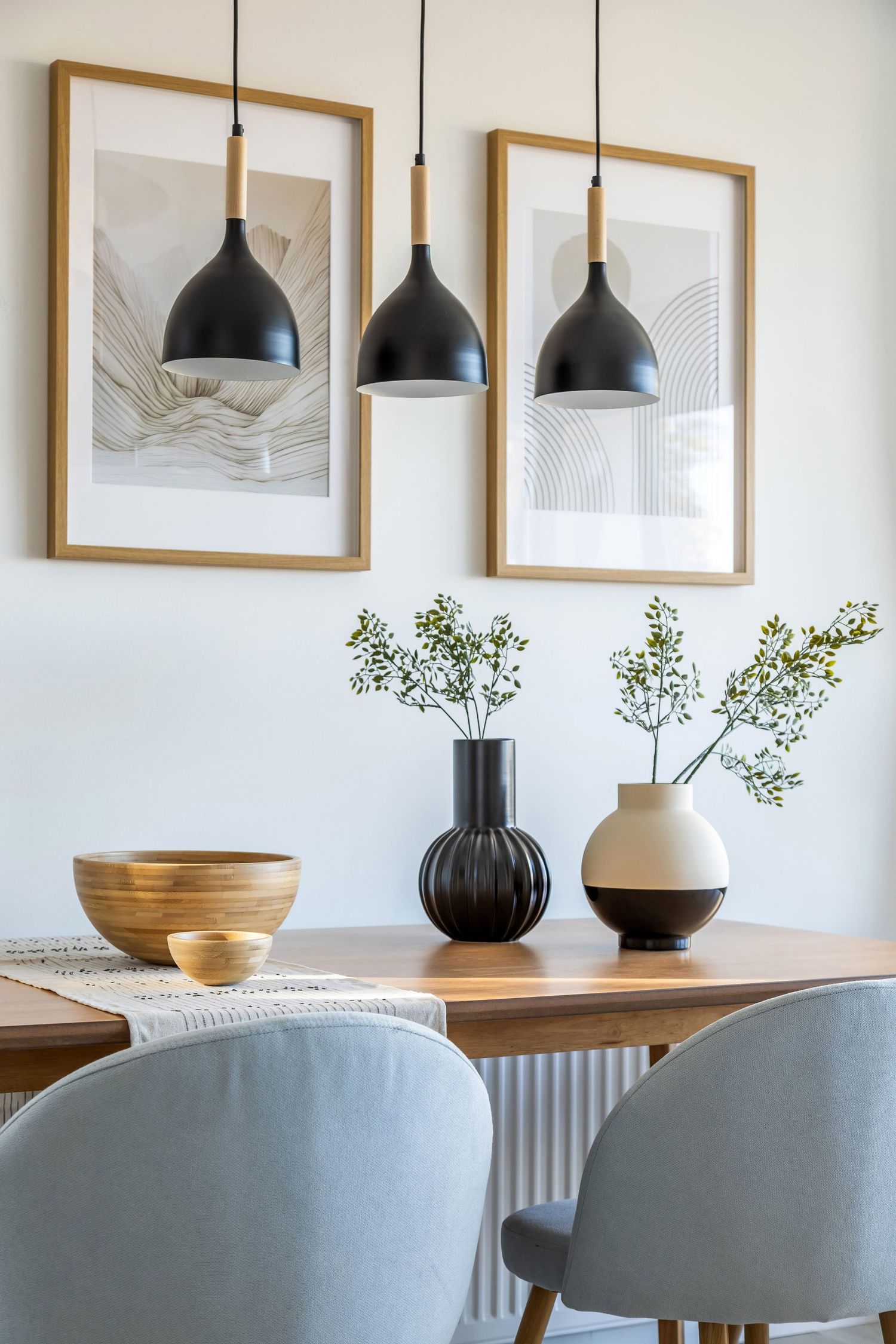 Scandinavian dining room with black pendant lights, wooden table, ceramic vases, and framed wall art.