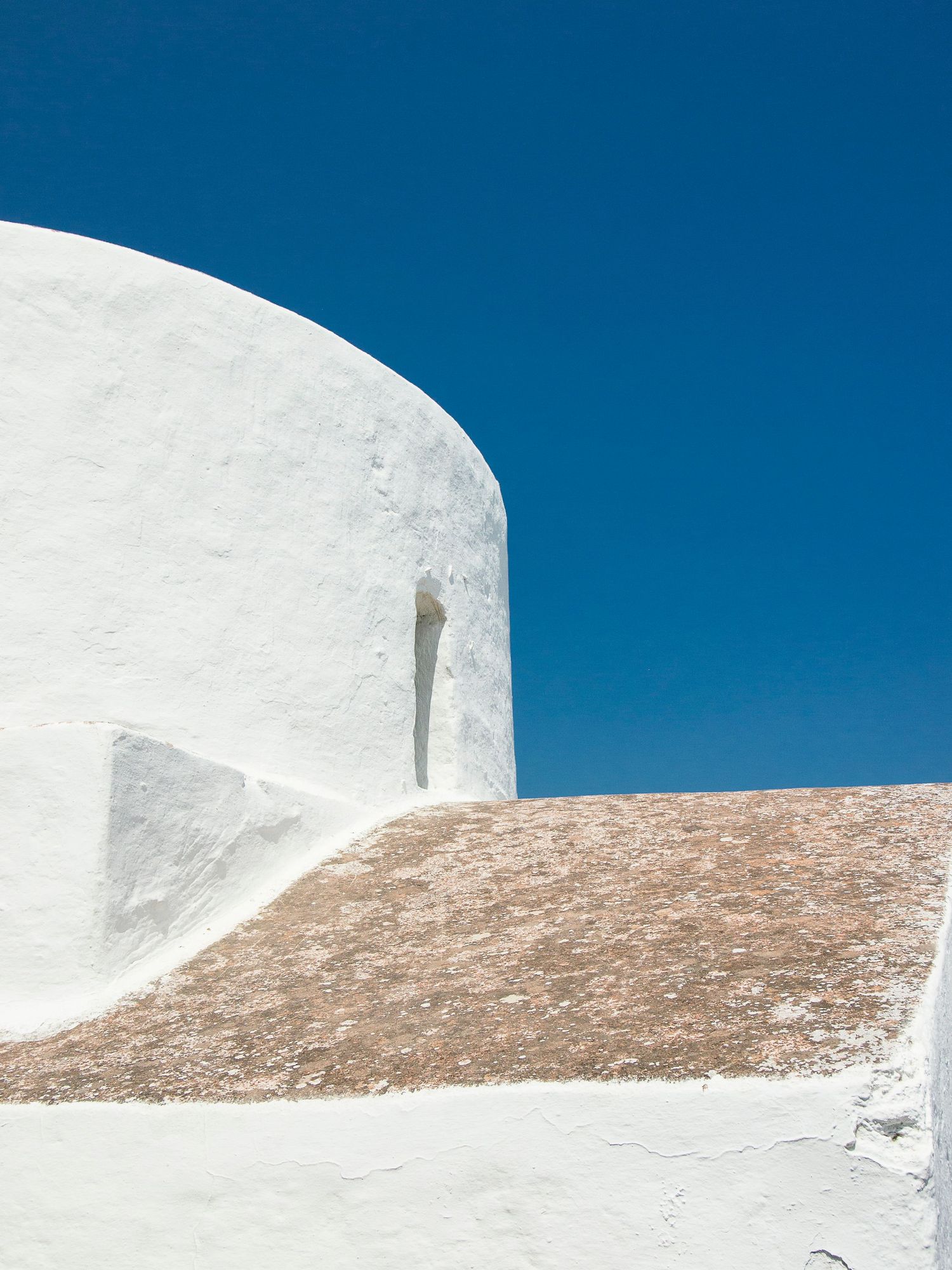 Whitewashed curved wall of a traditional Greek island building against a vivid deep blue sky.