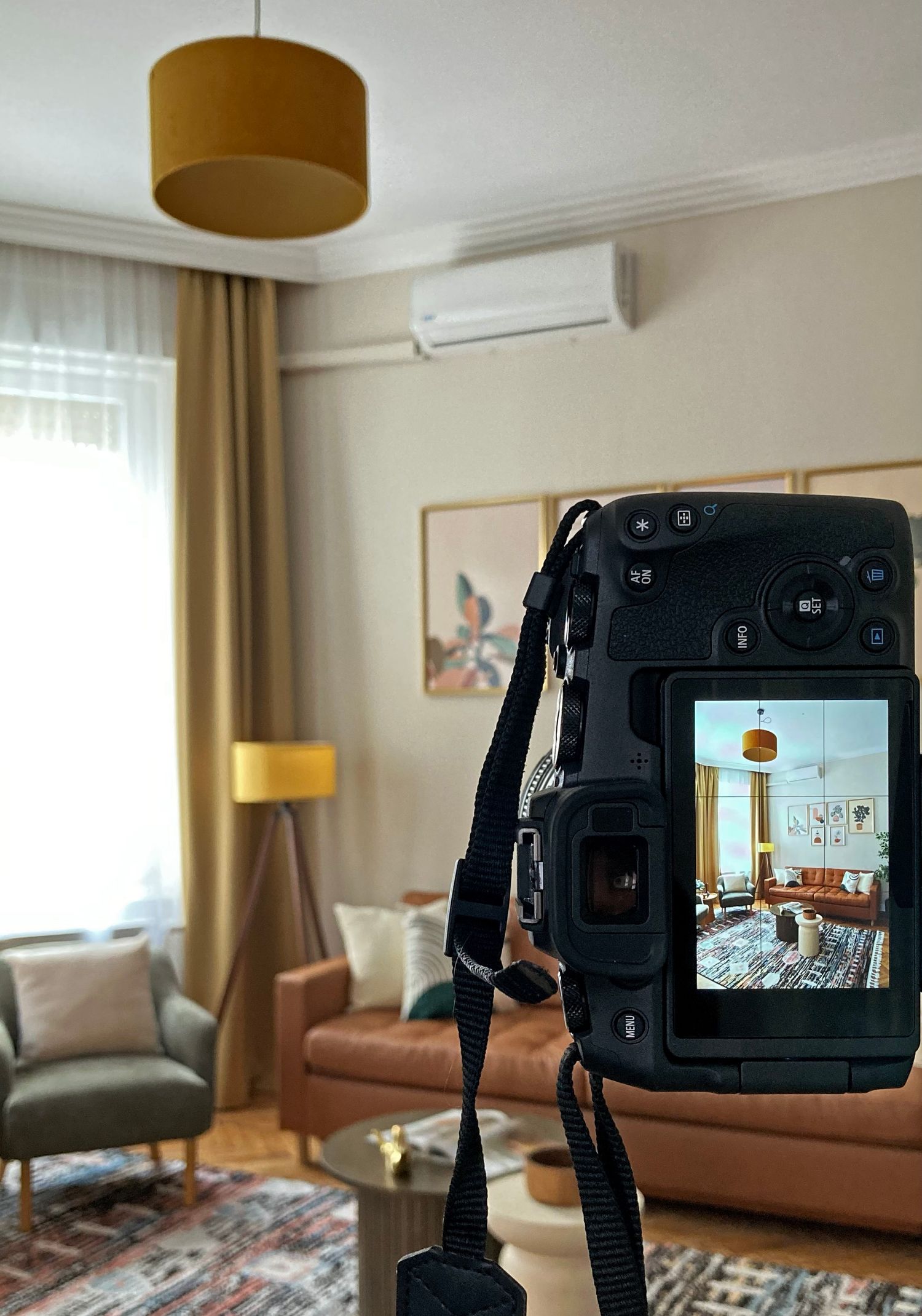 Professional camera on tripod capturing a warm-toned living room interior with orange sofa and curtains.