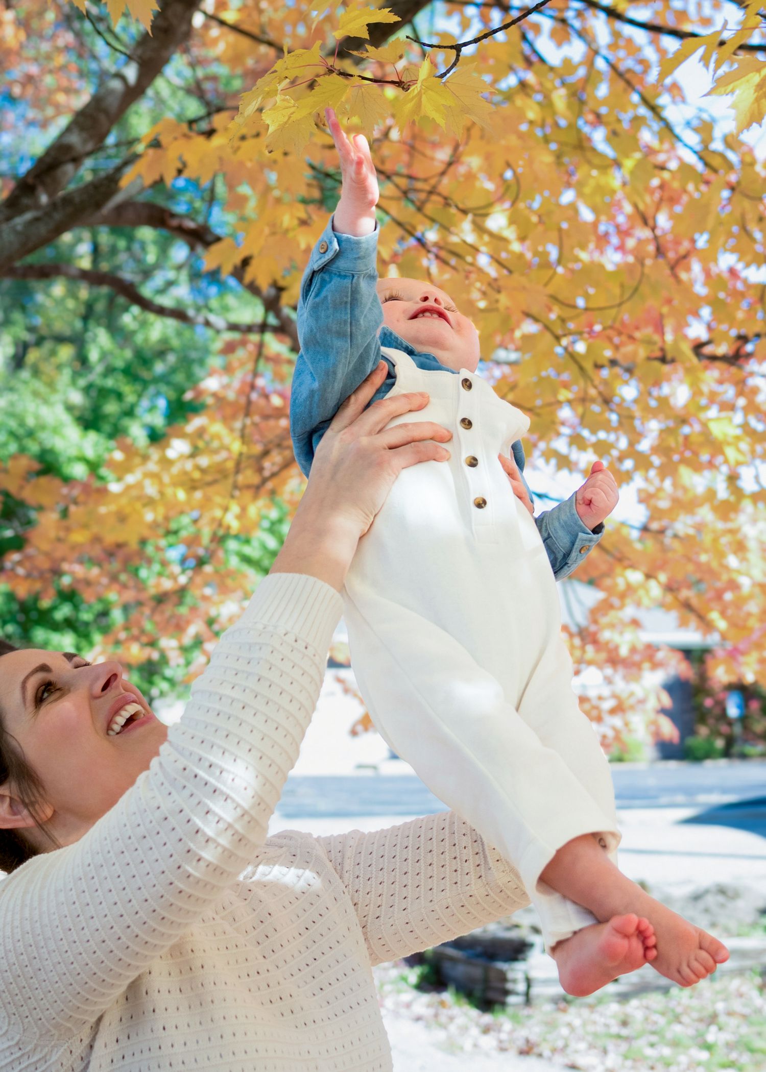 A person in a white knit sweater enjoying falling autumn leaves against a backdrop of golden foliage.