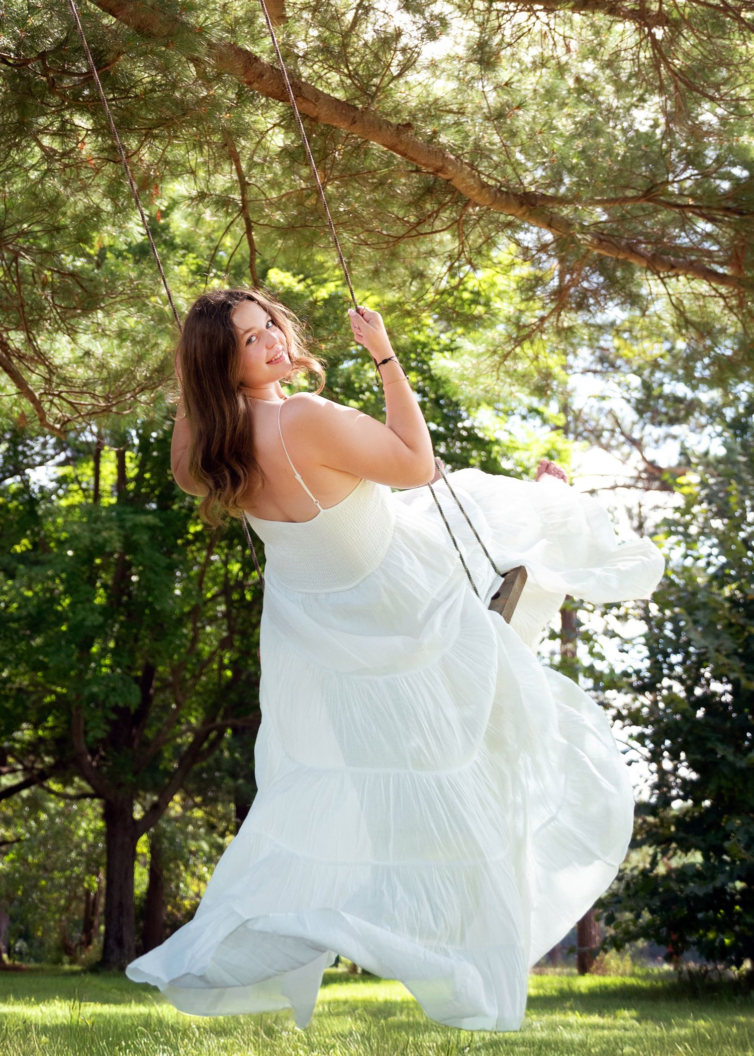 A graceful senior in a flowing white dress twirls joyfully outdoors under sunlit trees in a dynamic photo sequence.