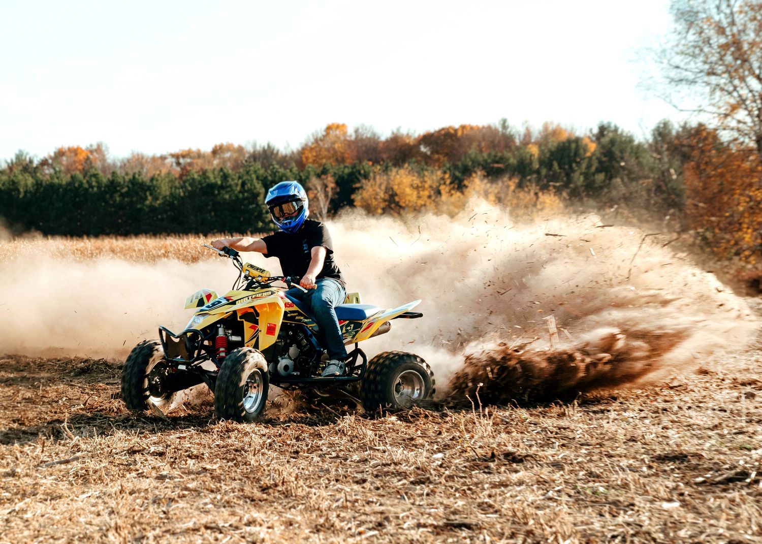 ATV rider kicks up dirt and dust while making a sharp turn on a yellow quad bike during off-road action.