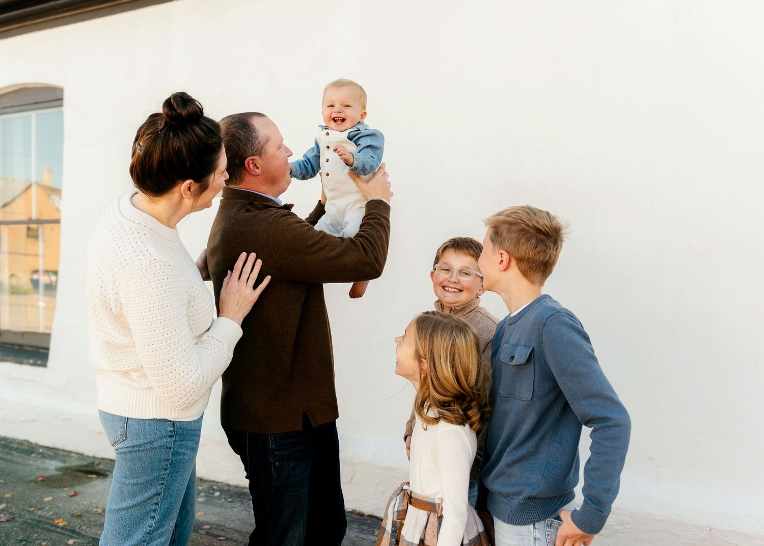 Family wearing coordinated blue and white outfits stands together outdoors during golden hour photo shoot.