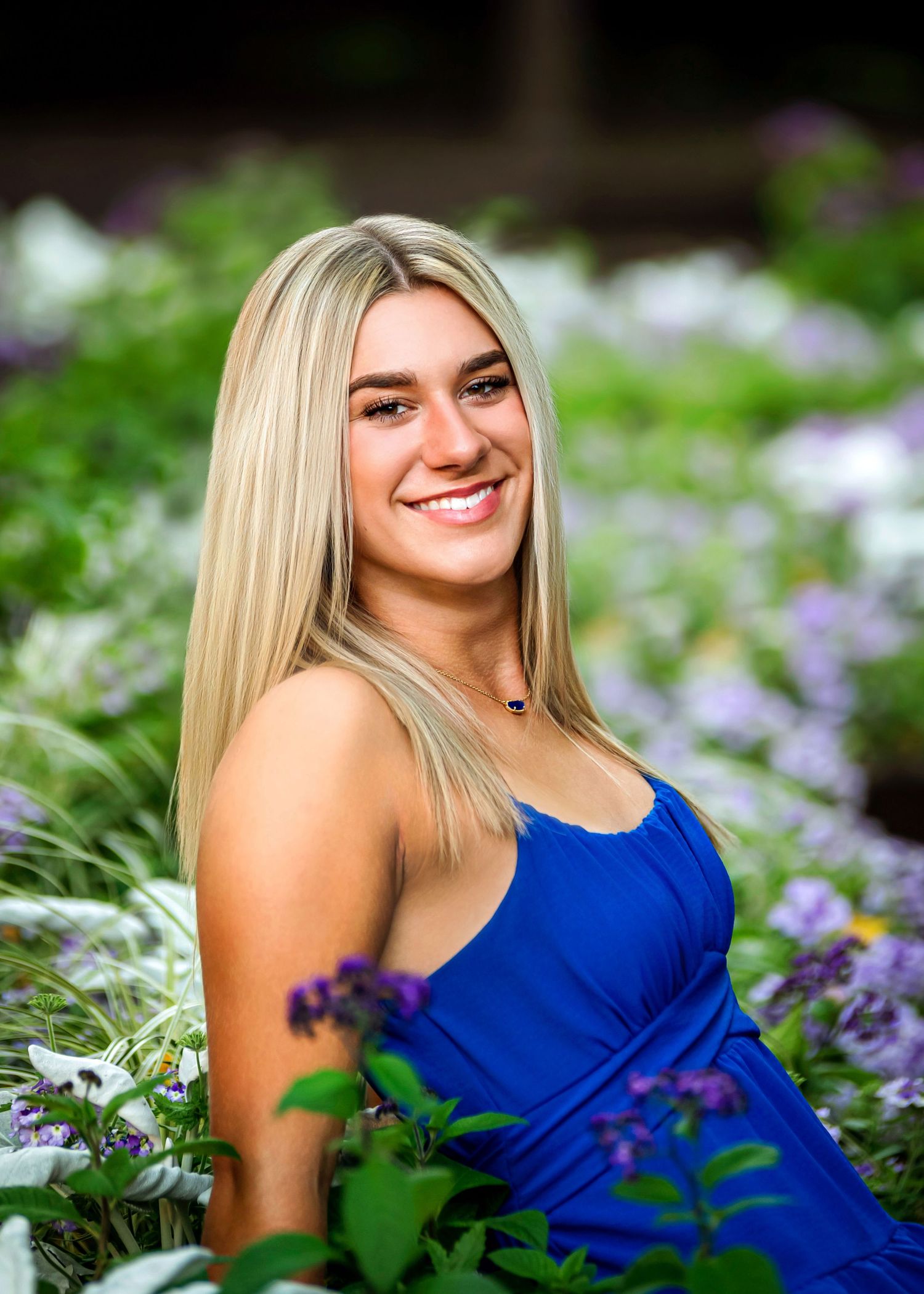 Person in royal blue dress poses among purple wildflowers during outdoor photo session.