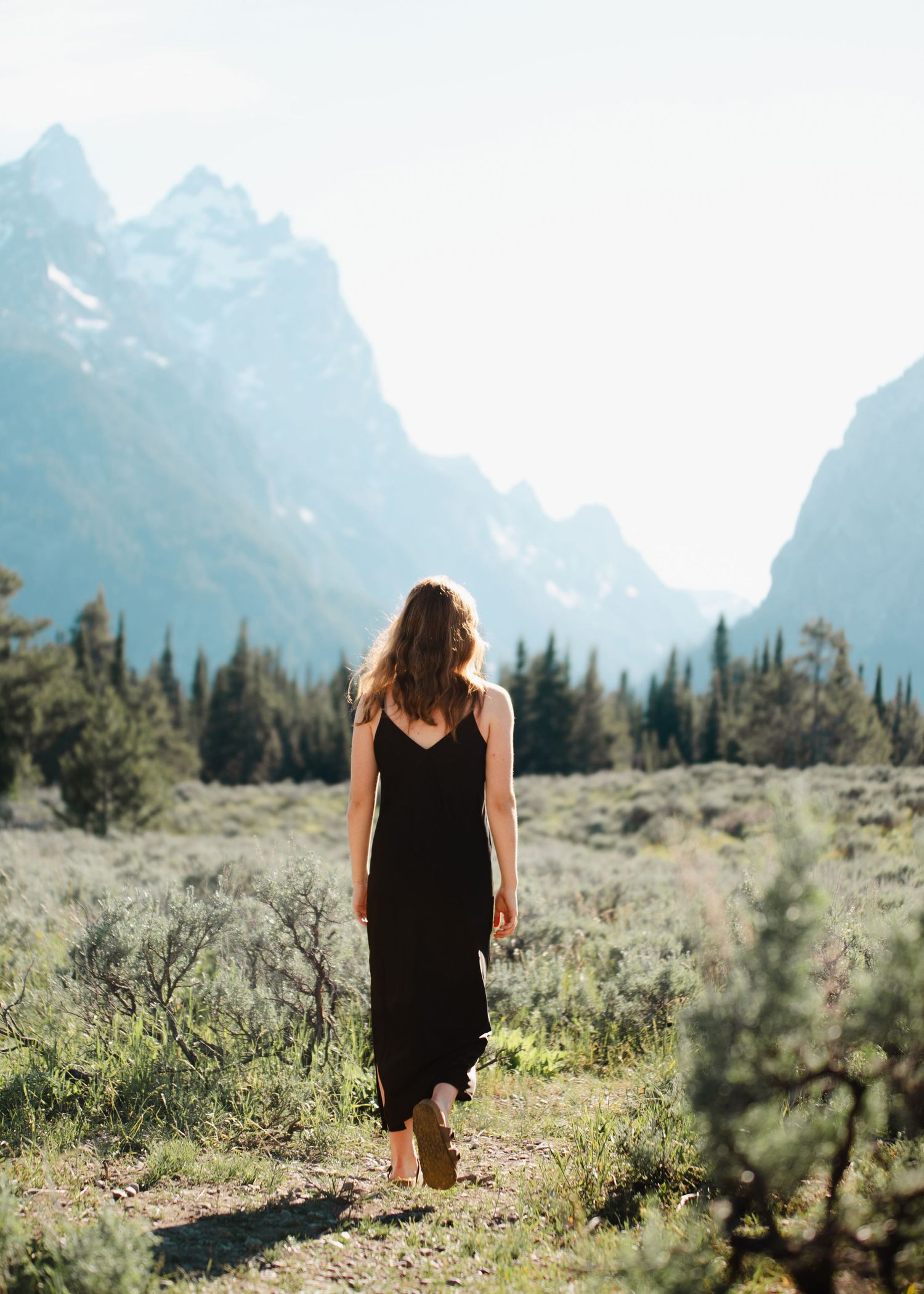 A senior picture of a girl walking in grassy terrain with majestic mountain peaks looming in the misty distance.
