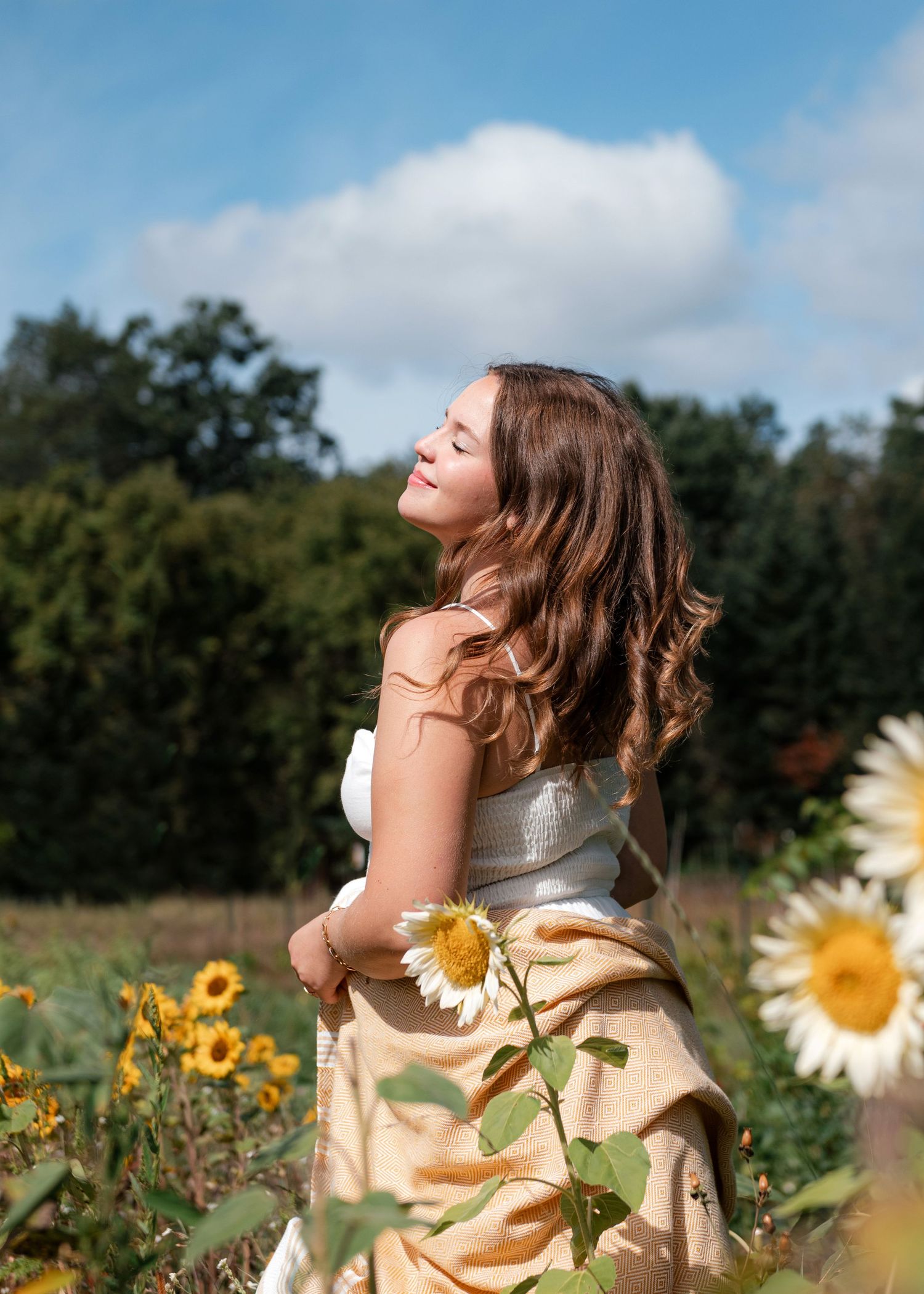 Person basking in sunlight amidst blooming sunflowers in a field on a bright summer day with blue sky and clouds.