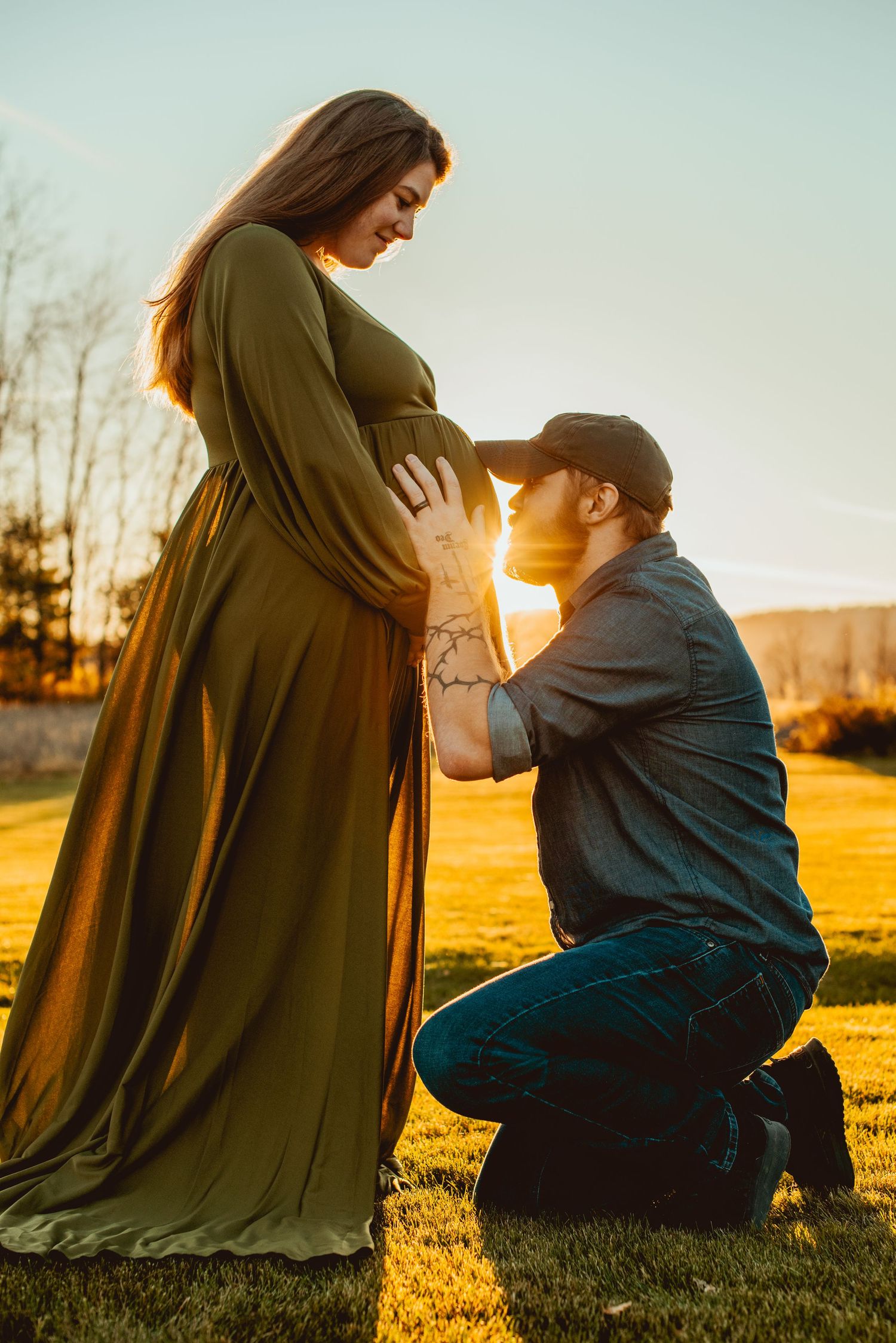 A tender maternity moment captured at sunset in a grassy field as an expectant couple shares an intimate moment.