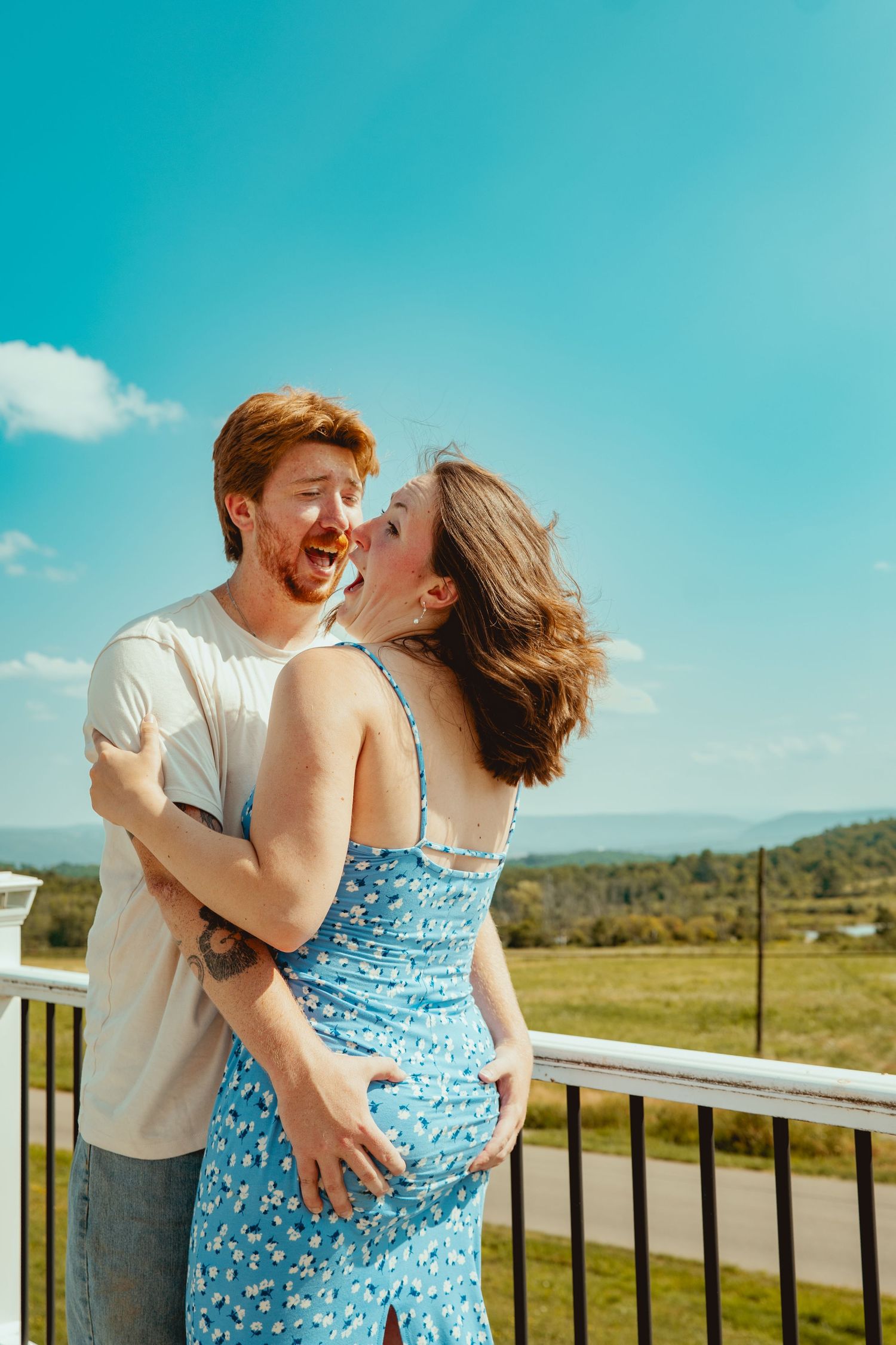 A couple shares a tender moment on a sunny balcony overlooking mountains and fields in a series of romantic photos.