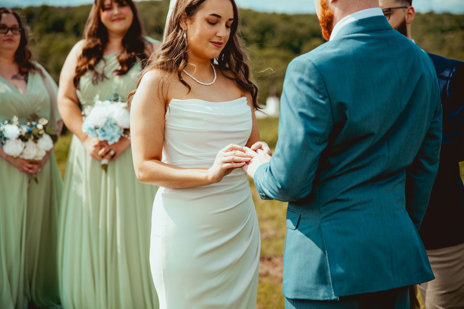 Wedding party in teal blue suits and mint green dresses pose together at an outdoor venue.