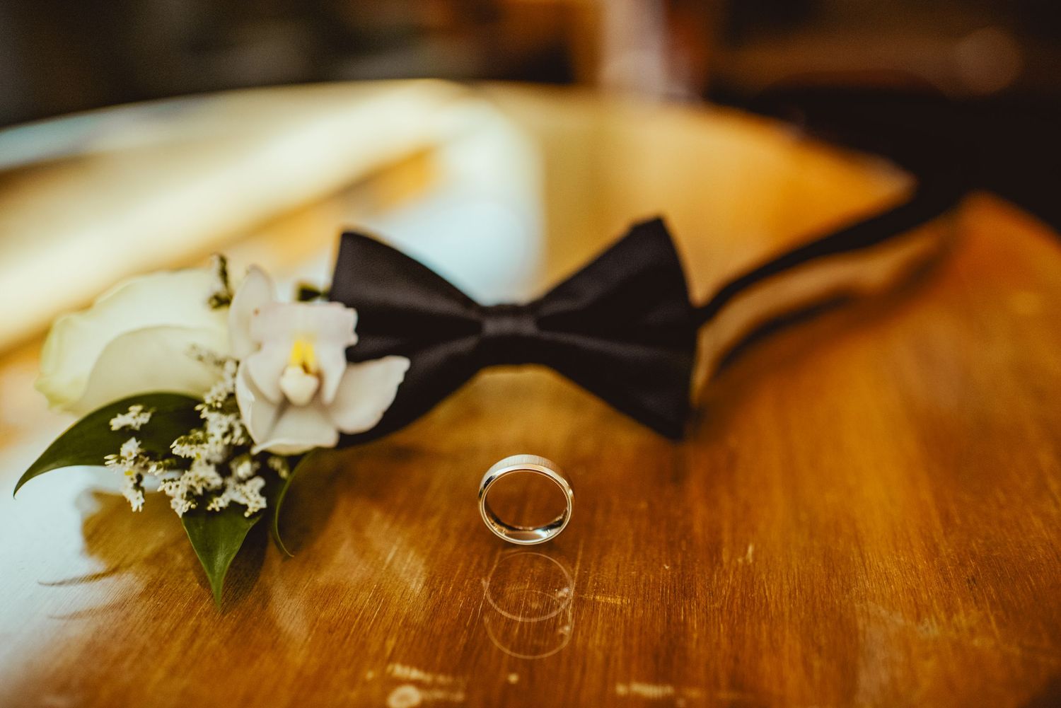 Wedding rings and white flower details on wooden surface in warm lighting.