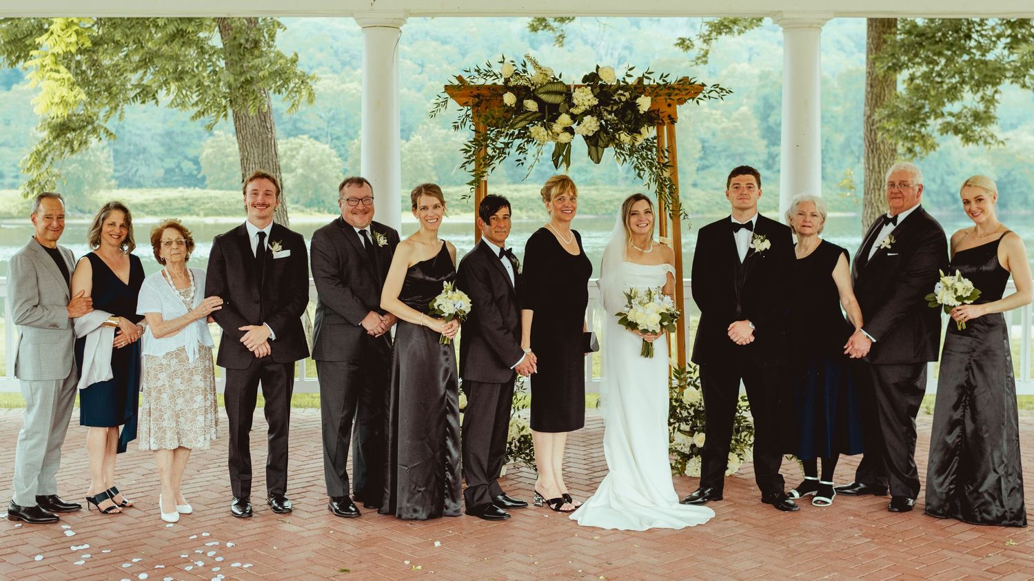 Panoramic shot of wedding party and guests lined up outdoors for formal photo.