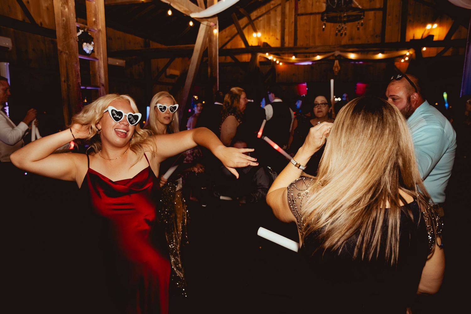 Dark reception venue with string lights showing silhouettes of wedding guests dancing and celebrating.