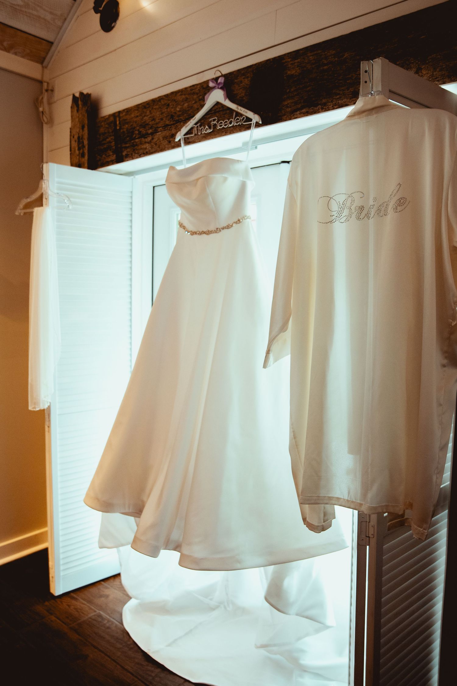 White strapless wedding gown and Bride robe hanging in a warmly lit dressing room.