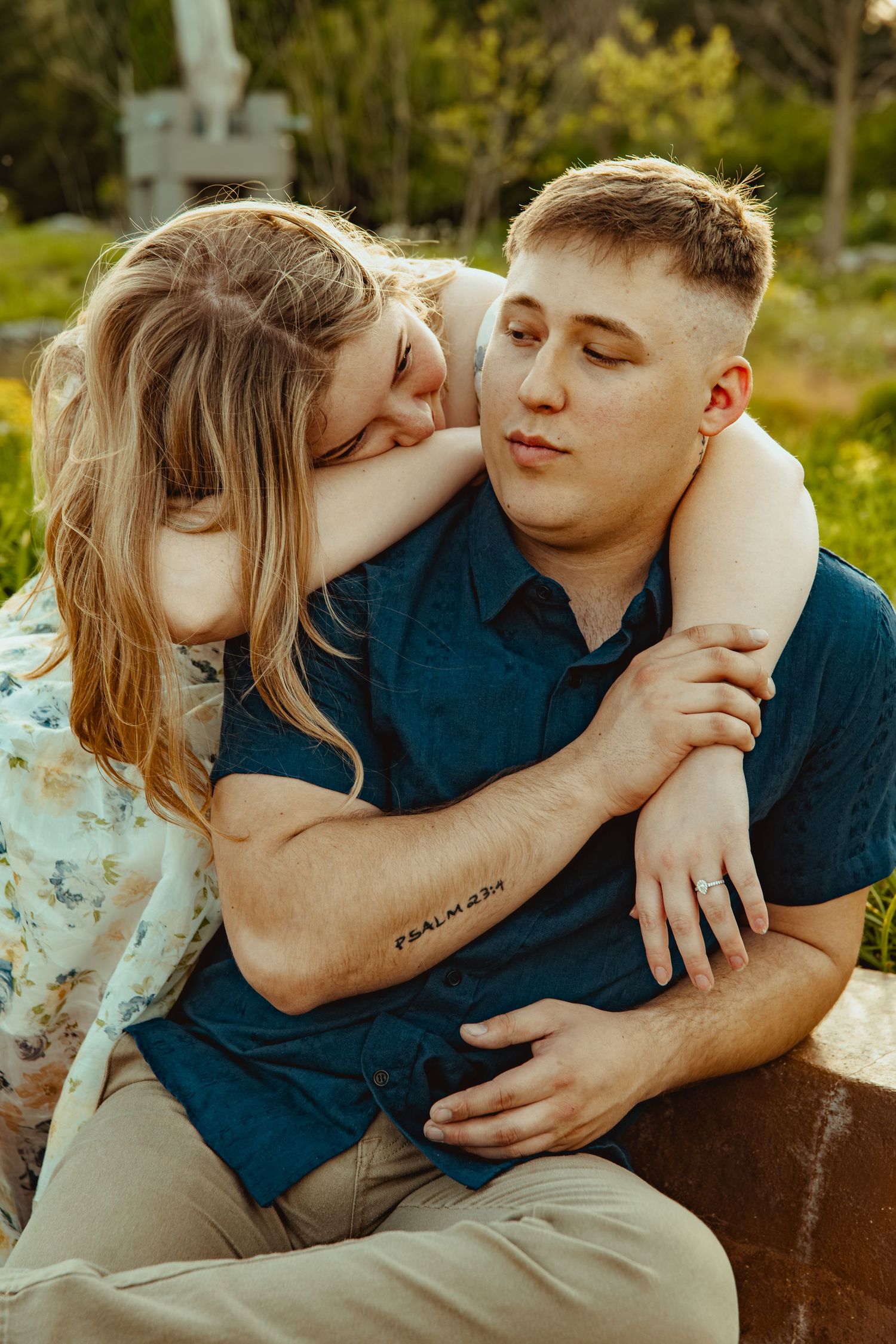 A young couple shares a tender moment outdoors, with a woman resting her head on a mans shoulder while embracing him.