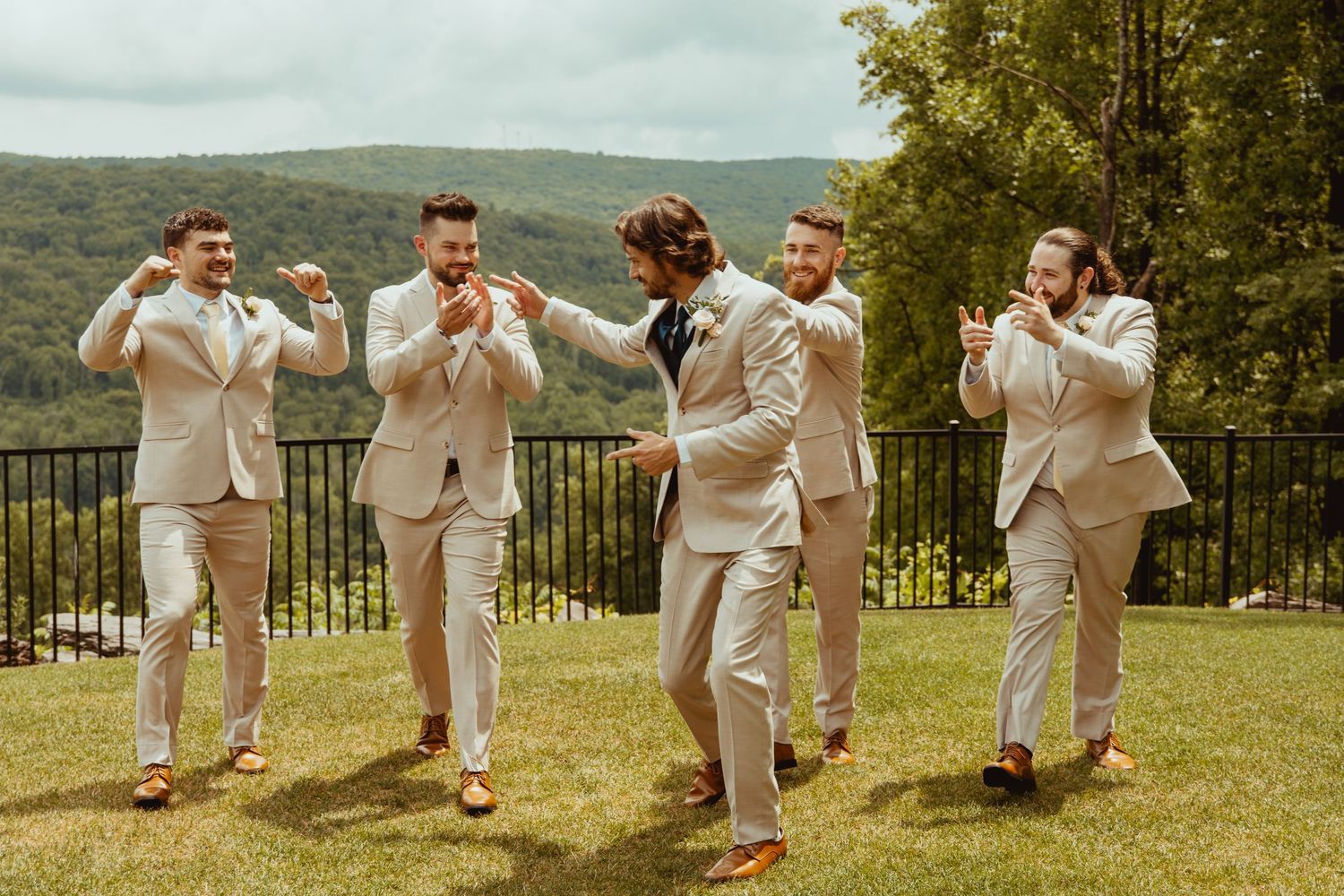 Groom and groomsmen in tan suits celebrating outdoors with mountains in background at wedding.