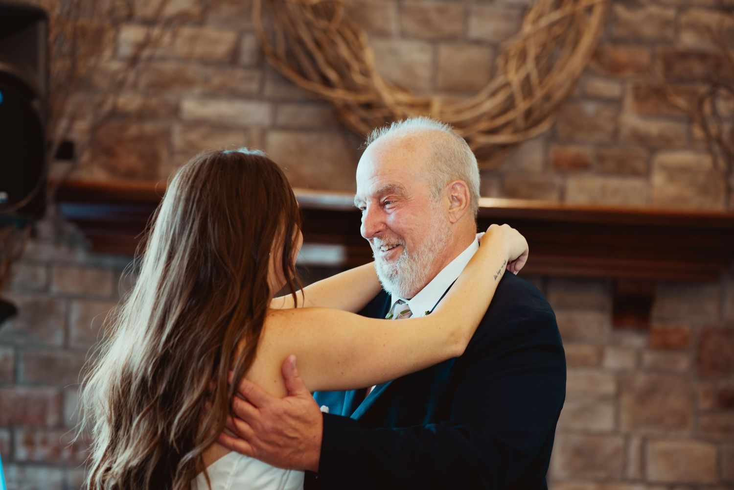 Elderly man smiling while dancing with a young woman in a white dress at a wedding reception.