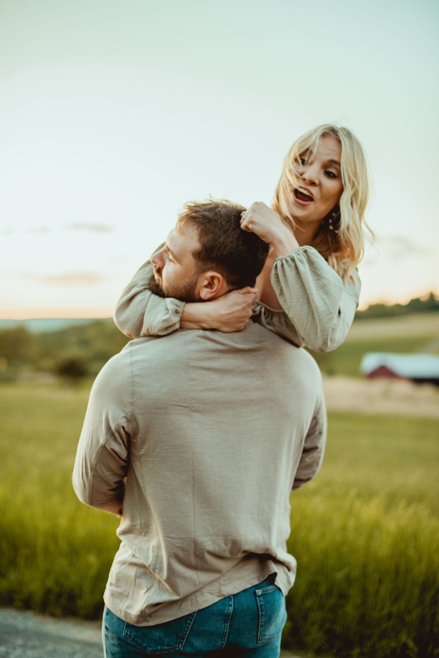 A couple embraces and laughs together in a grassy field with soft lighting.