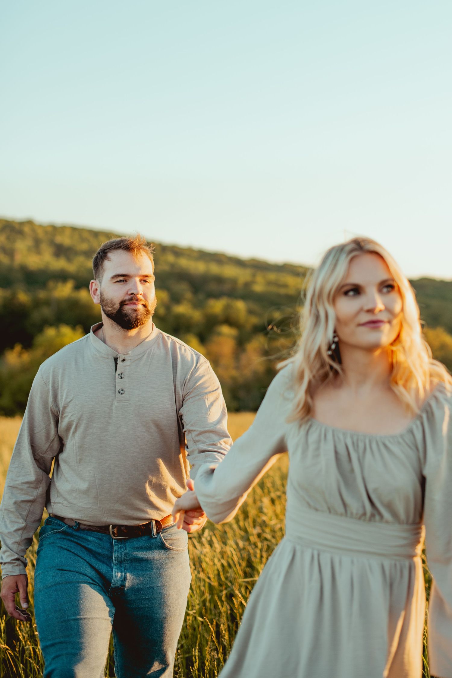 A couple poses together in a golden field at sunset wearing casual attire.